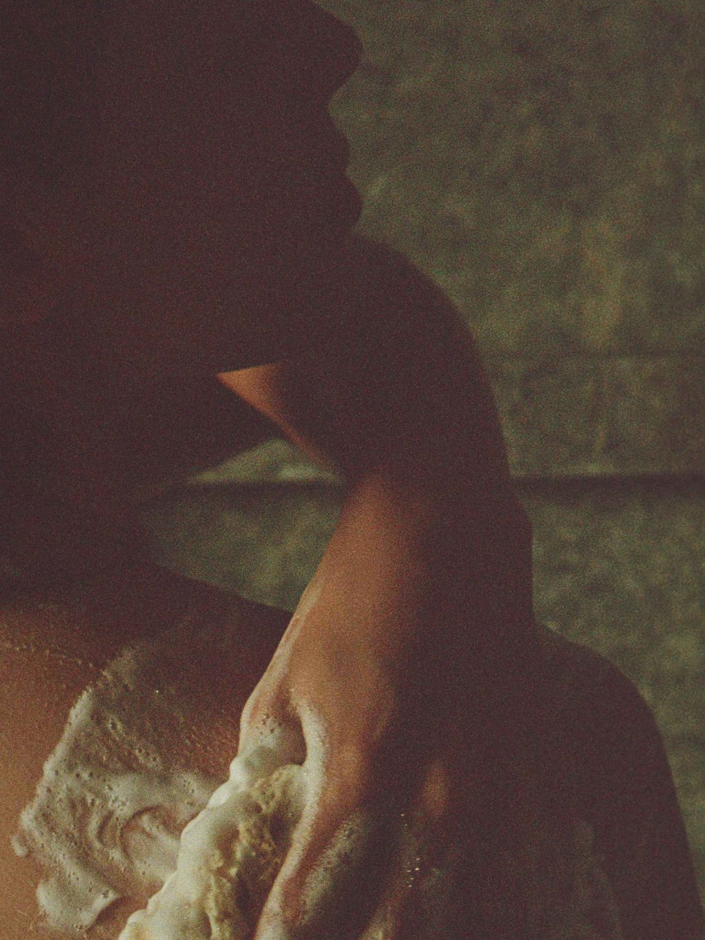 Person washing a shoulder with a textured sponge in a softly lit shower