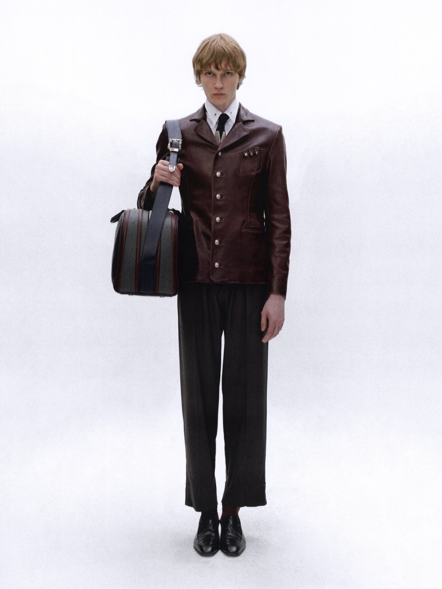 Full length model in a burgundy leather jacket with a tie holding a striped bag