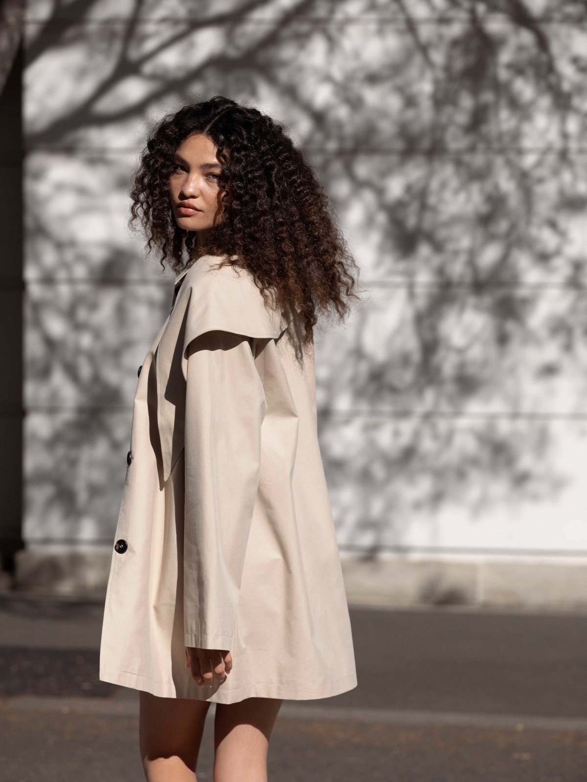 Model in a pale coat on a sunlit city street