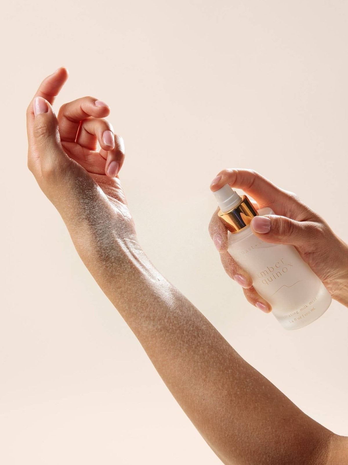 Hand spraying a golden capped face mist onto an outstretched forearm