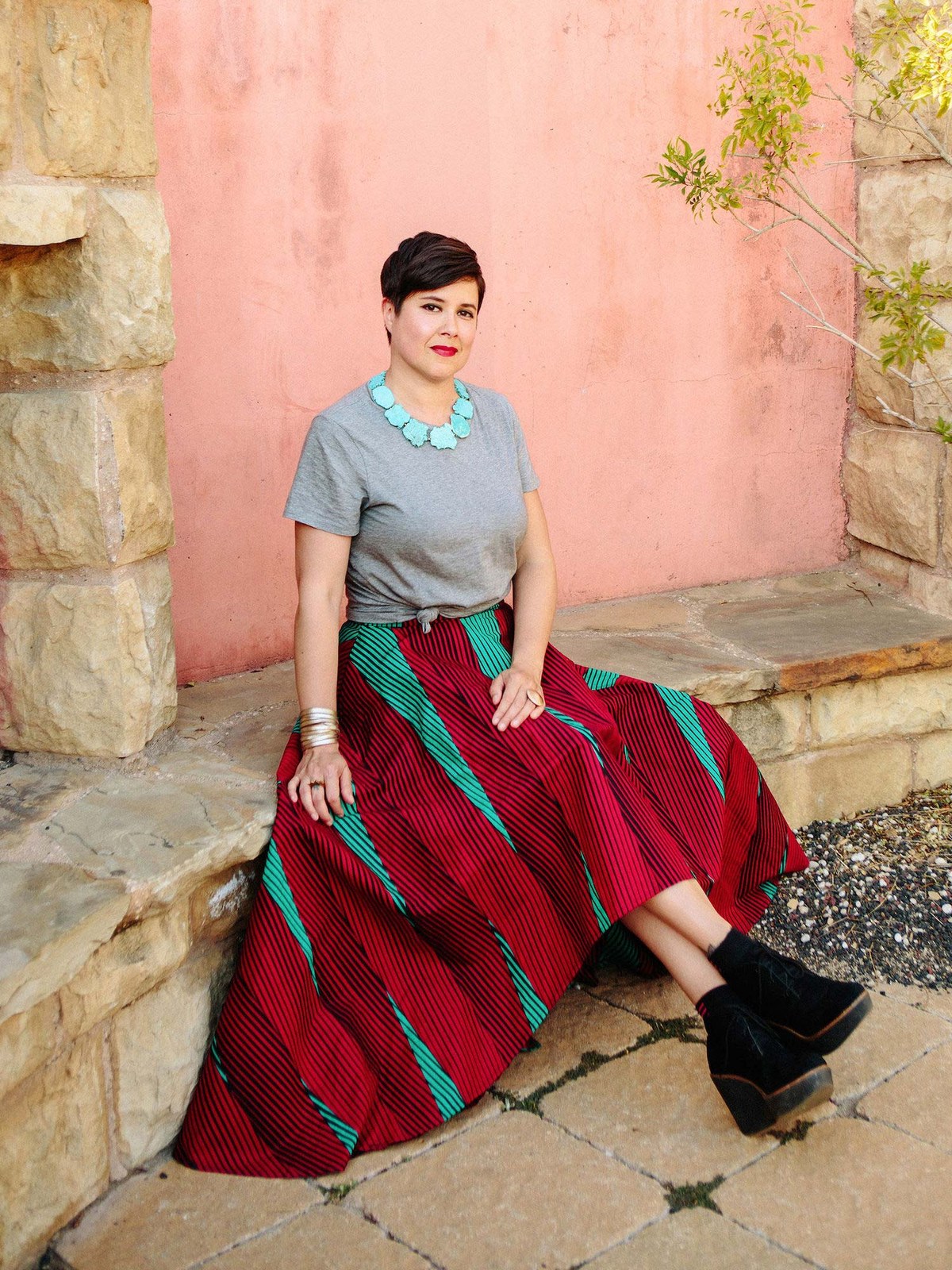 Sandra Velasquez seated outside in a gray top, turquoise necklace and colorful skirt