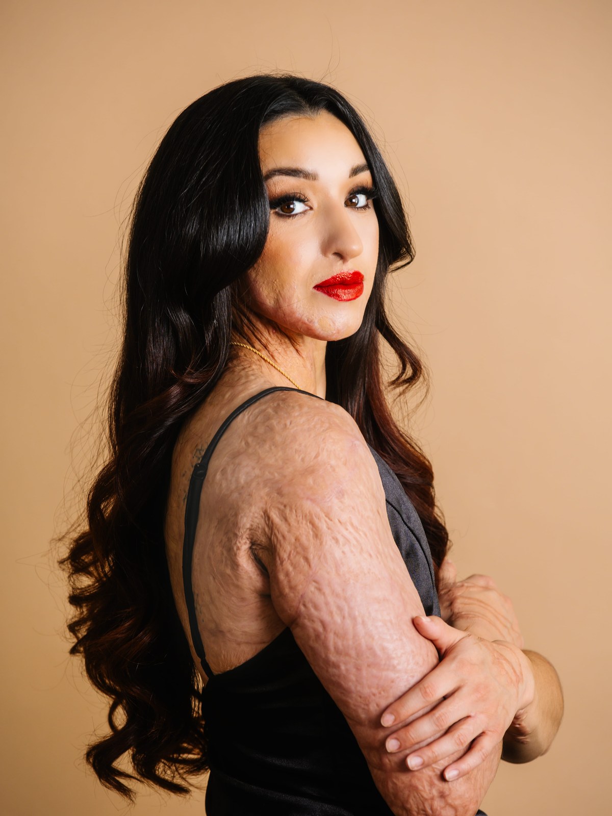 A woman in a black dress against a peach studio backdrop