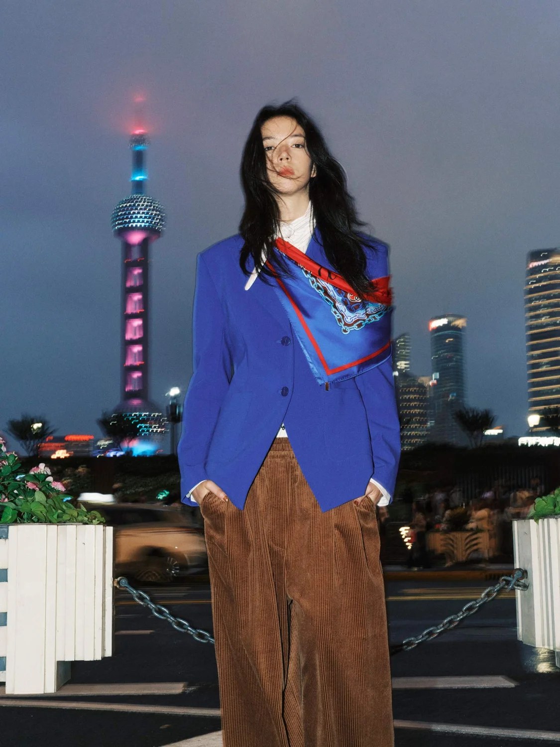 Model in a blue blazer and brown trousers against the night skyline