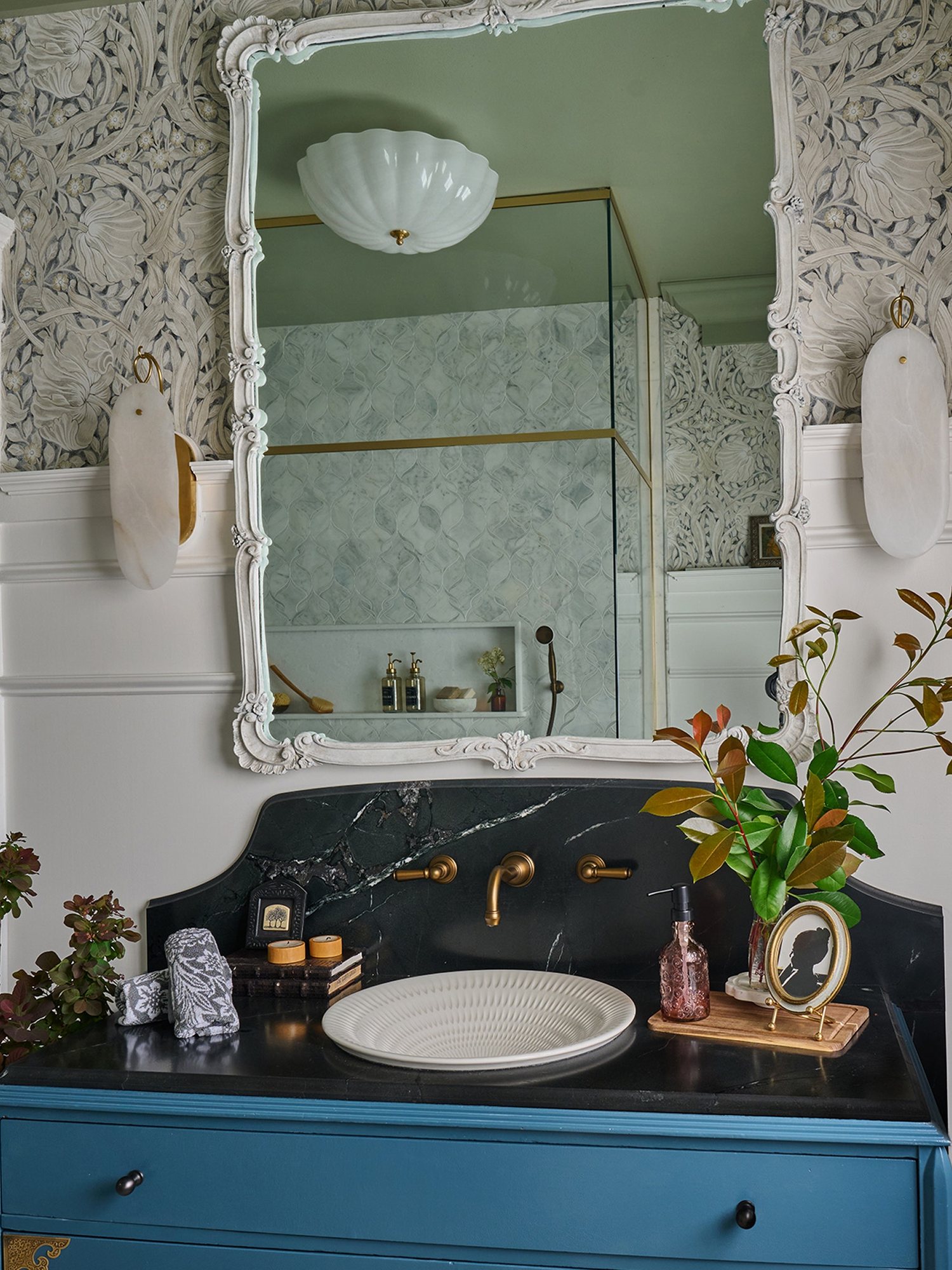 Bathroom with white sconces, an ornate mirror and a blue vanity