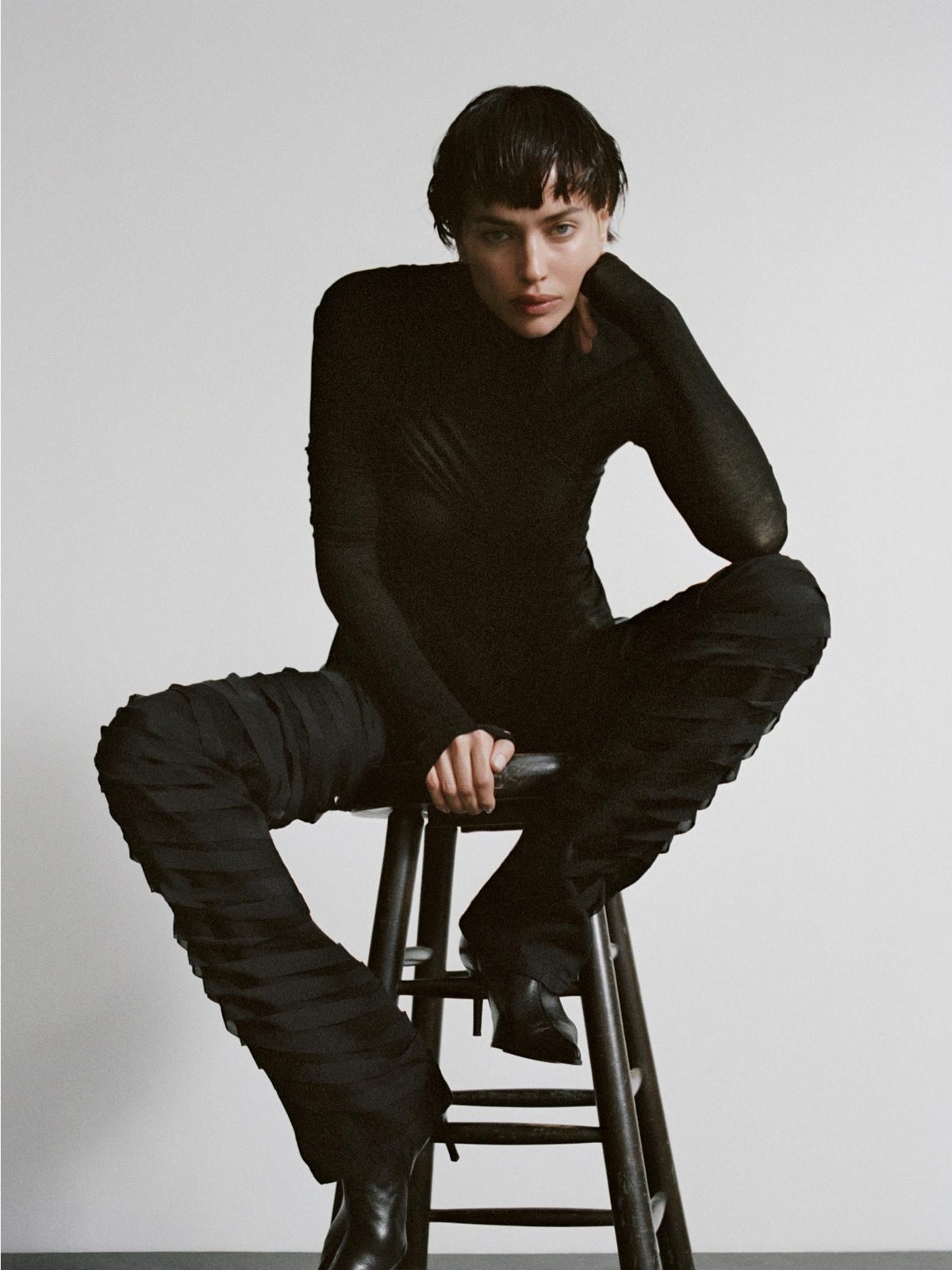 Irina Shayk seated in a sculptural black outfit and pointed shoes