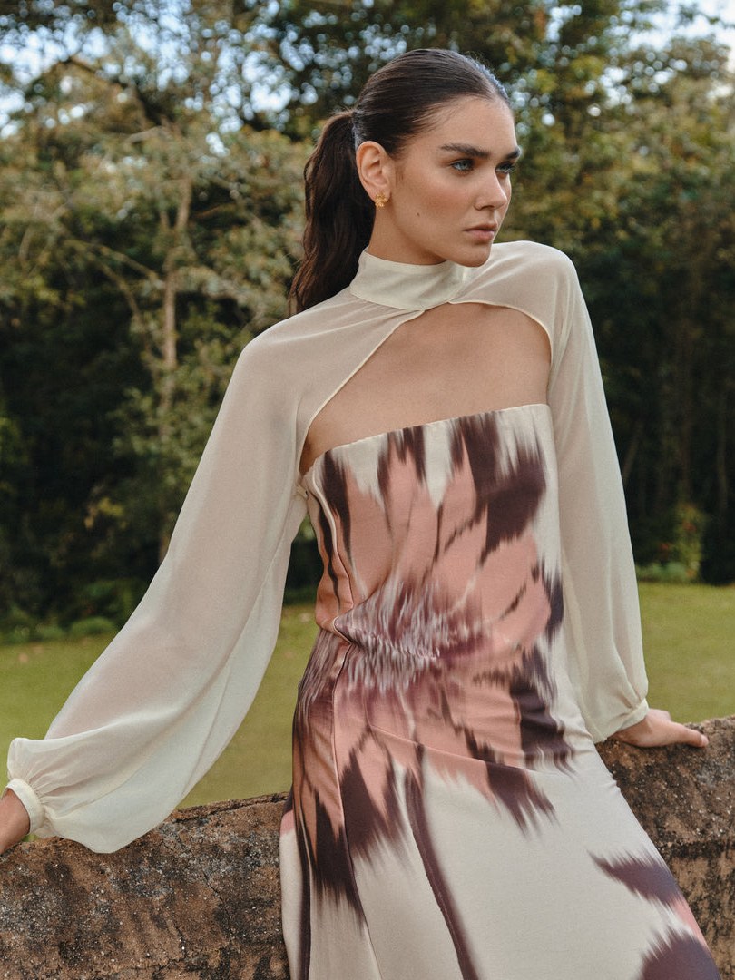 Woman in a mauve printed dress with a sheer cape in a garden.