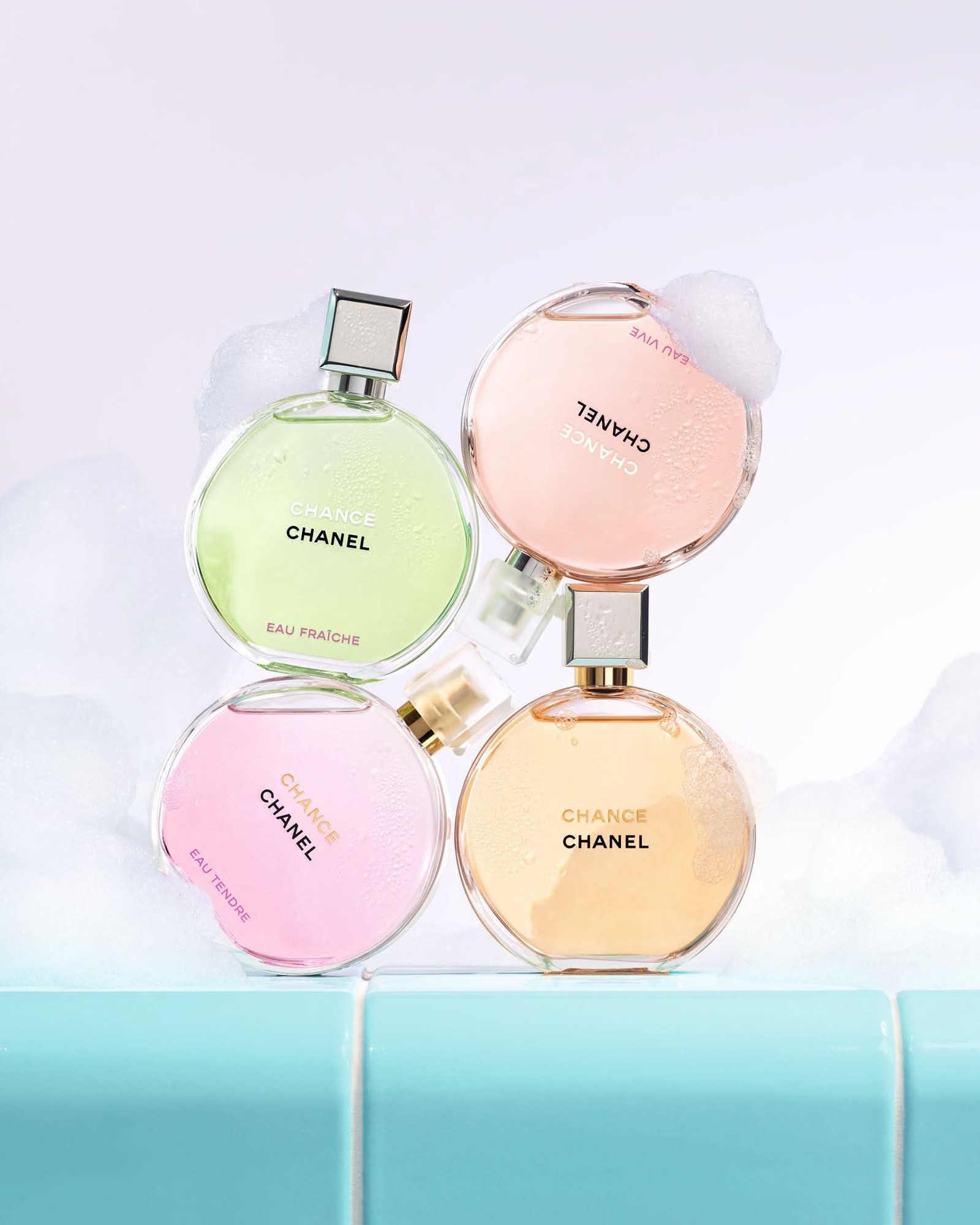 Four round Chanel Chance bottles stacked in soap foam on teal tiles, in green Eau Fraîche, pink Eau Tendre, peach Eau Vive and golden original