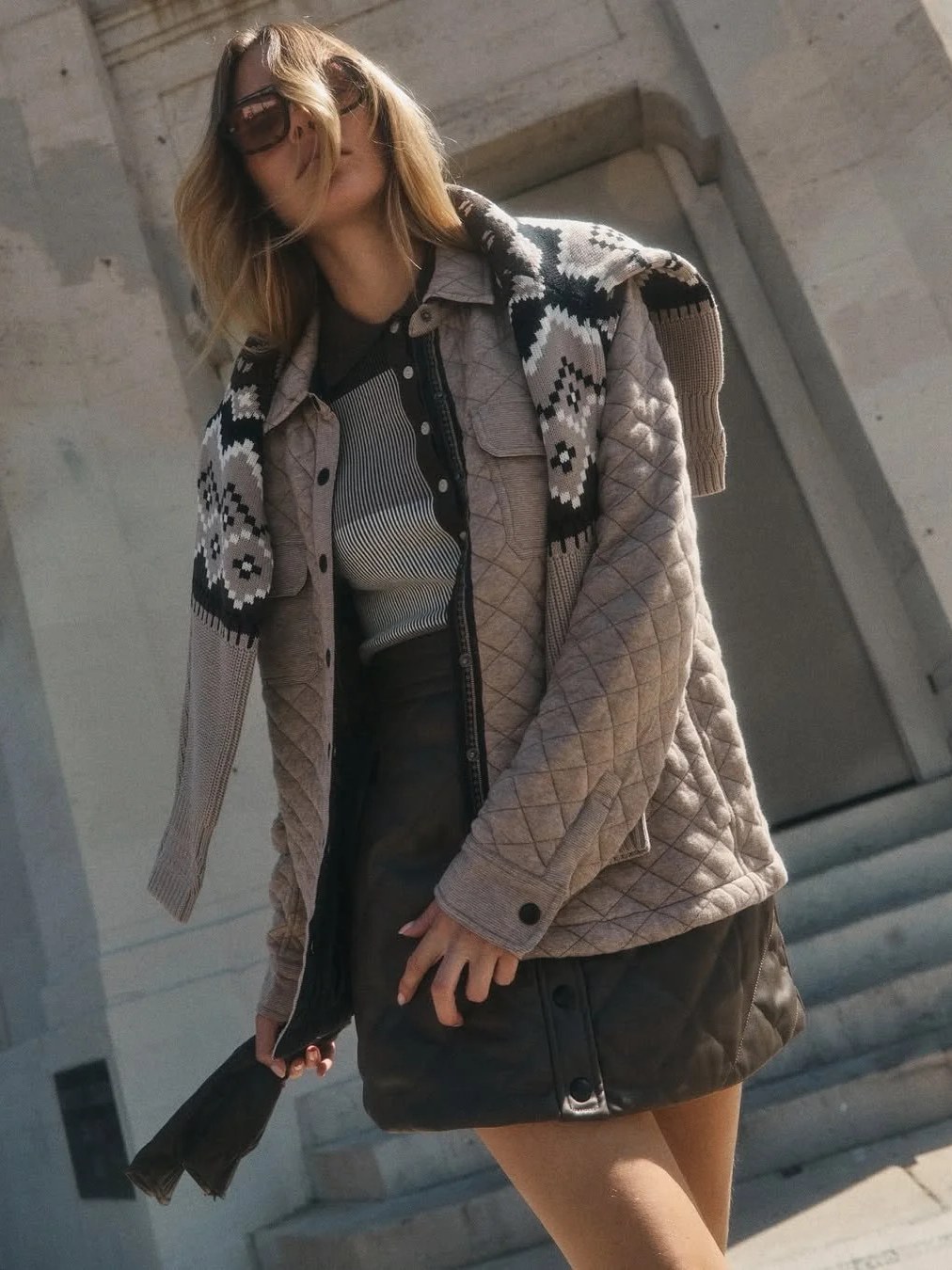 Model in a patterned sweater and quilted jacket on outdoor steps