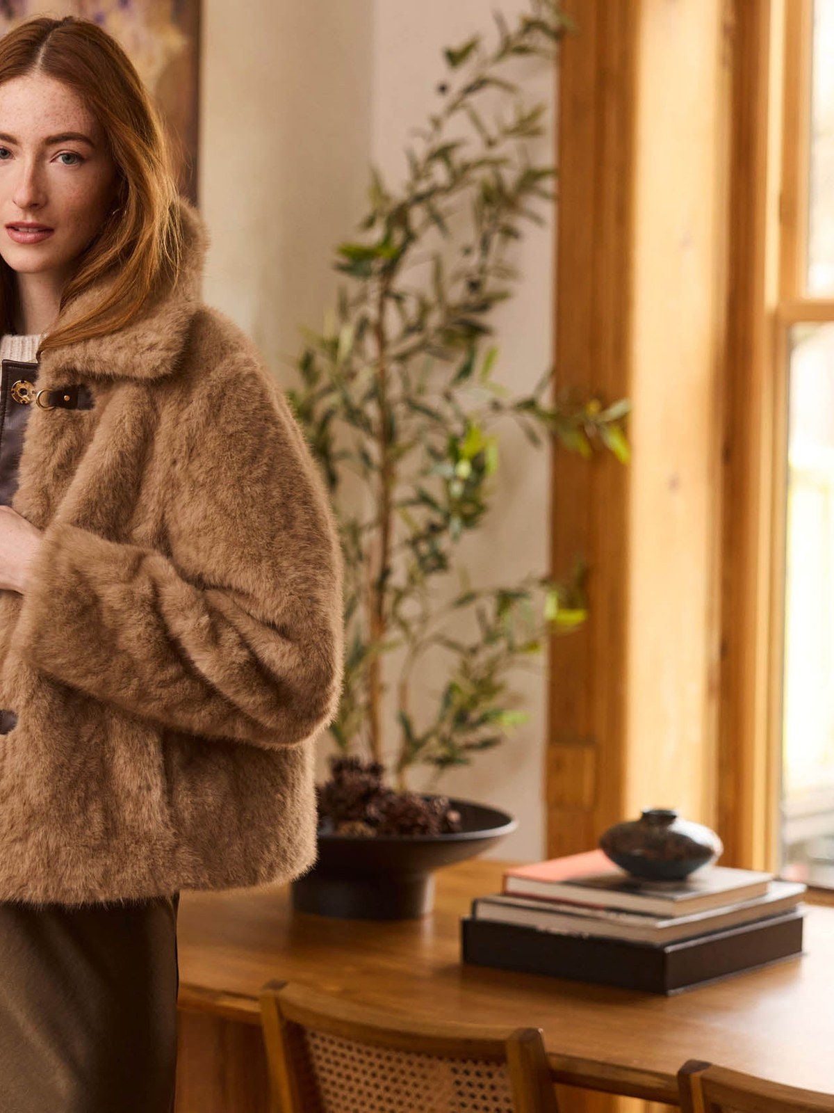 Model in a plush tan Heartloom jacket beside a wood table