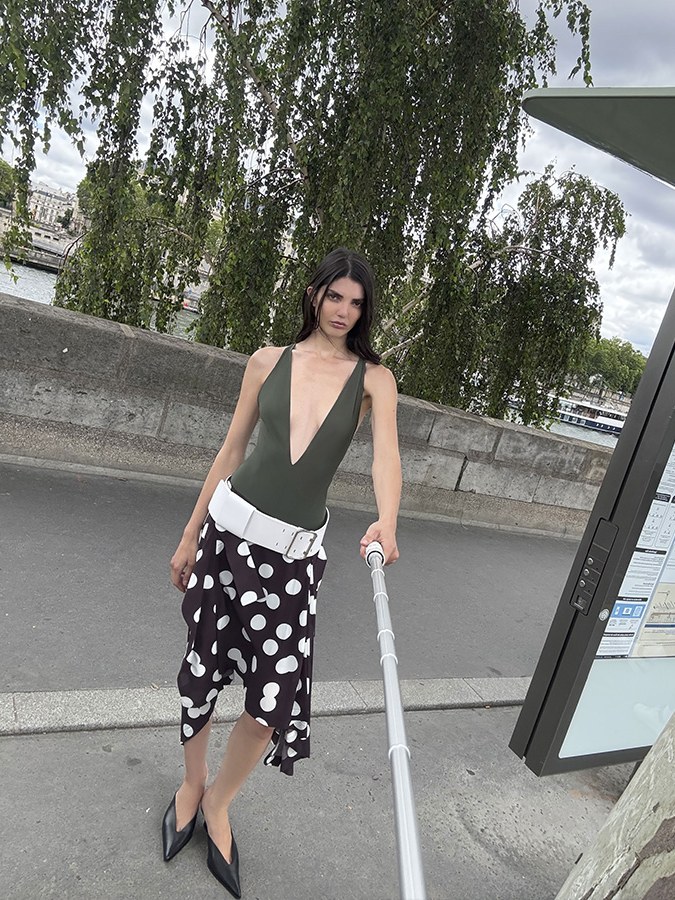 Model in an olive top and spotted skirt by a riverside