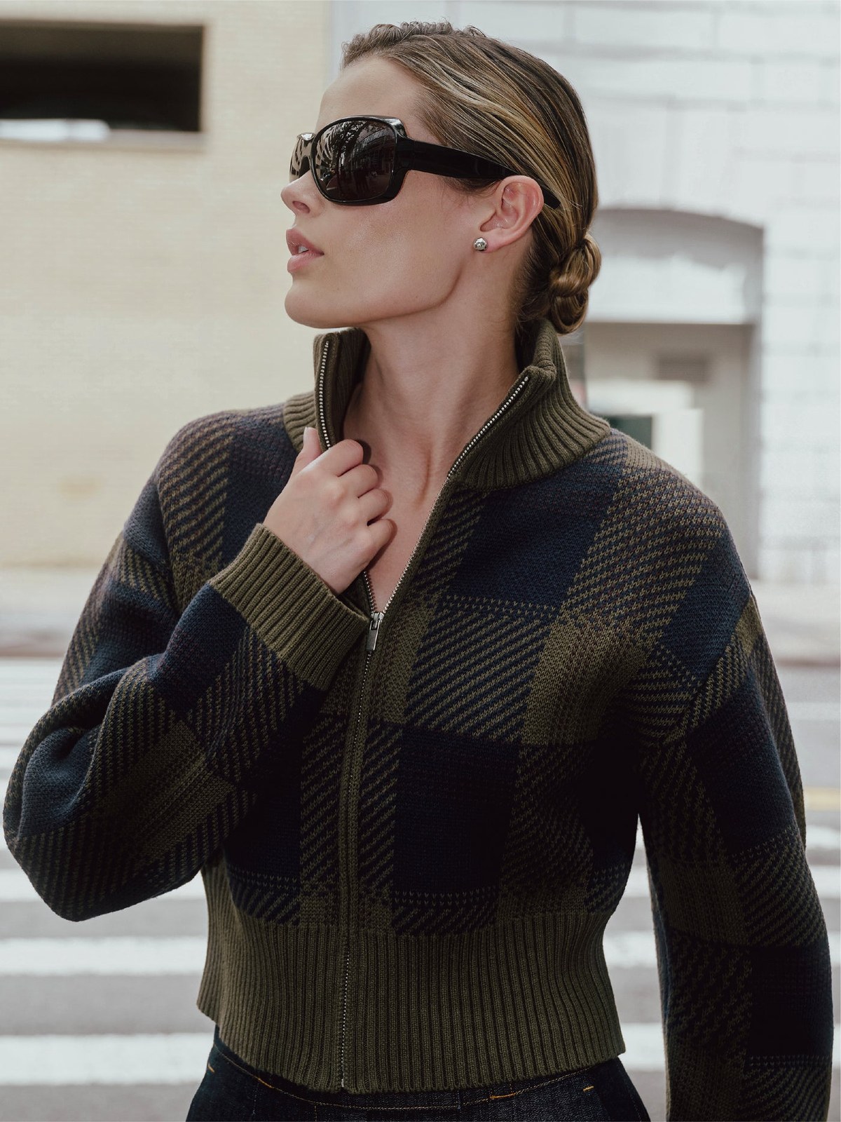 Model in a dark plaid knit and sunglasses against a city facade