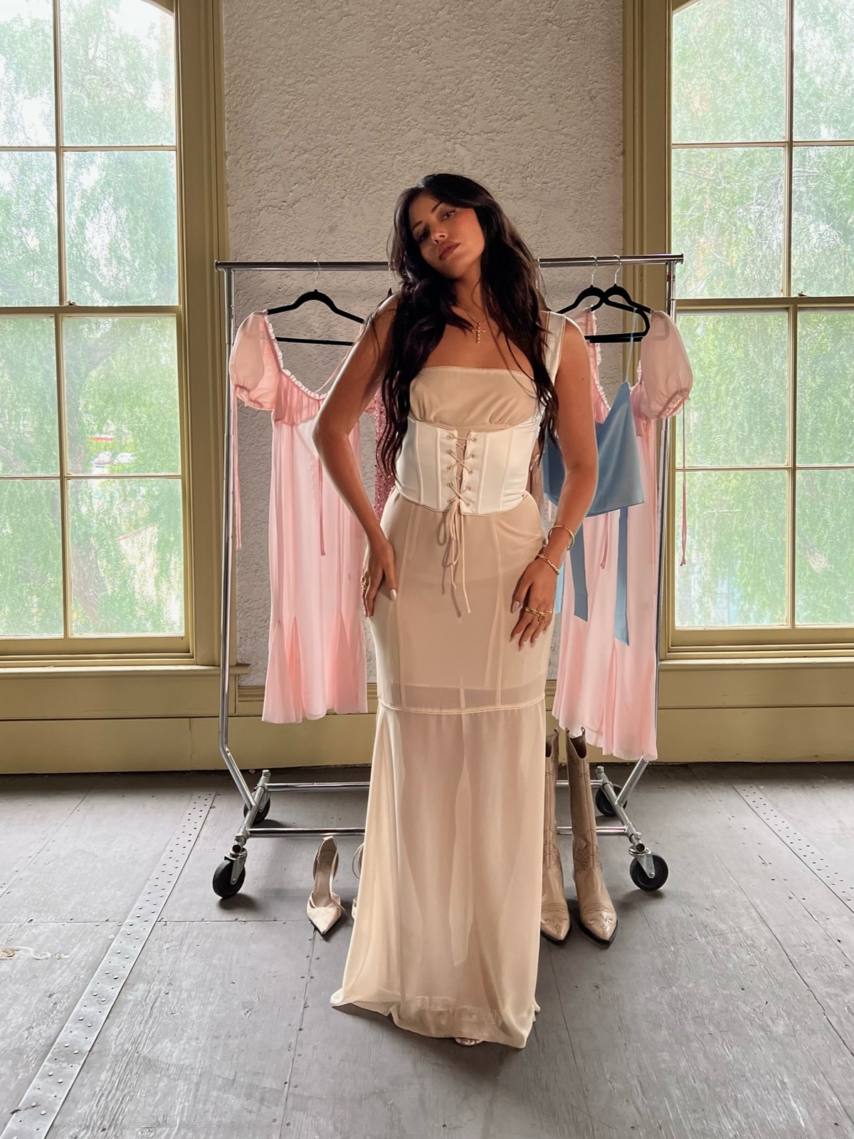 Model in an ivory corset dress in a styled studio beside a clothing rack
