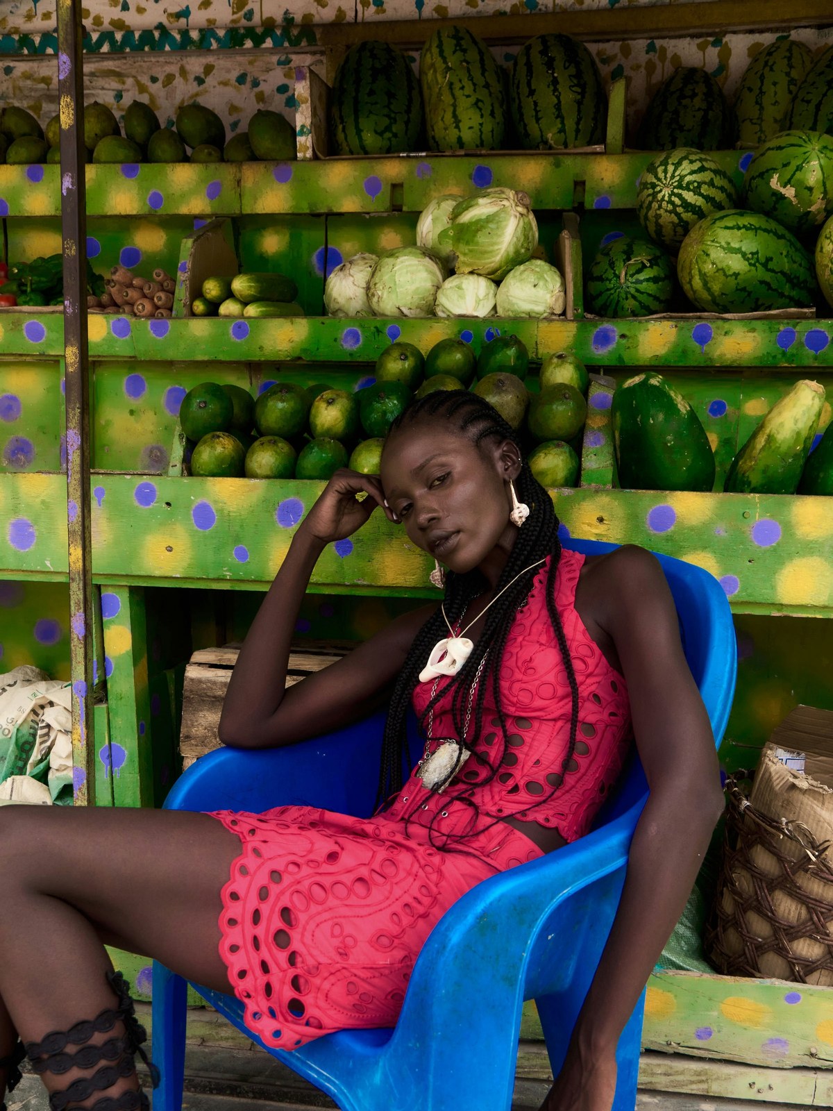 Model in a red embroidered dress seated in a colorful Zanzibar fruit market