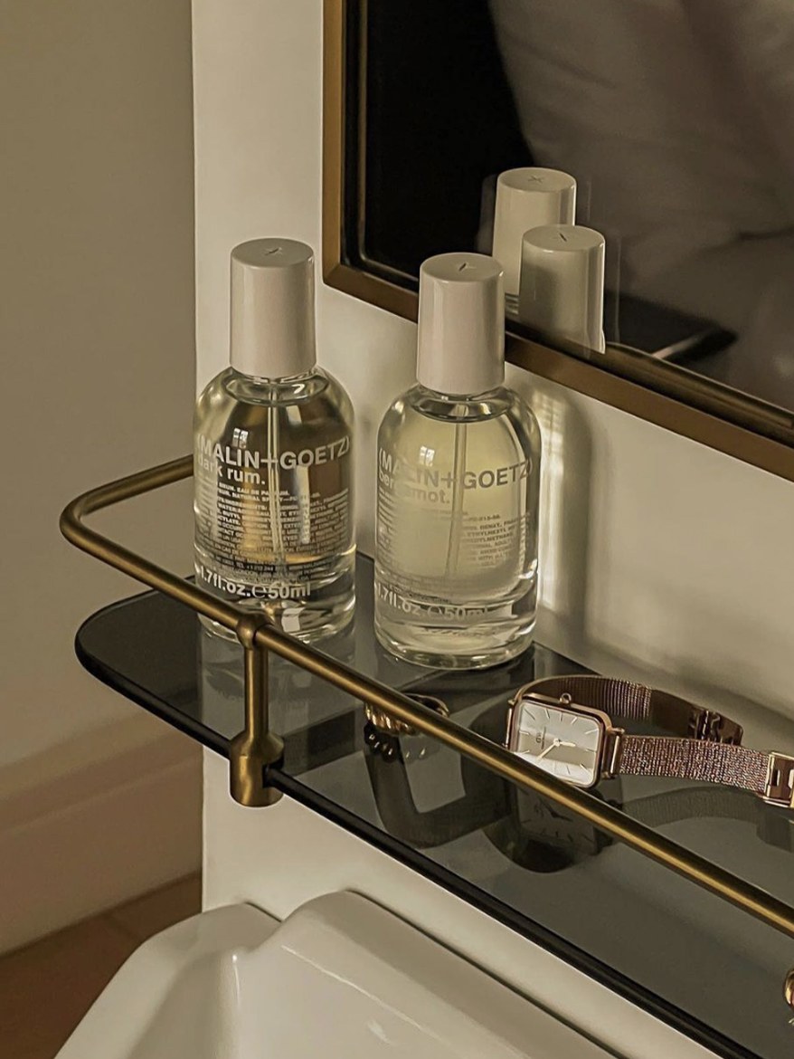 Two fragrance bottles arranged on a glass bathroom shelf beside a mirror