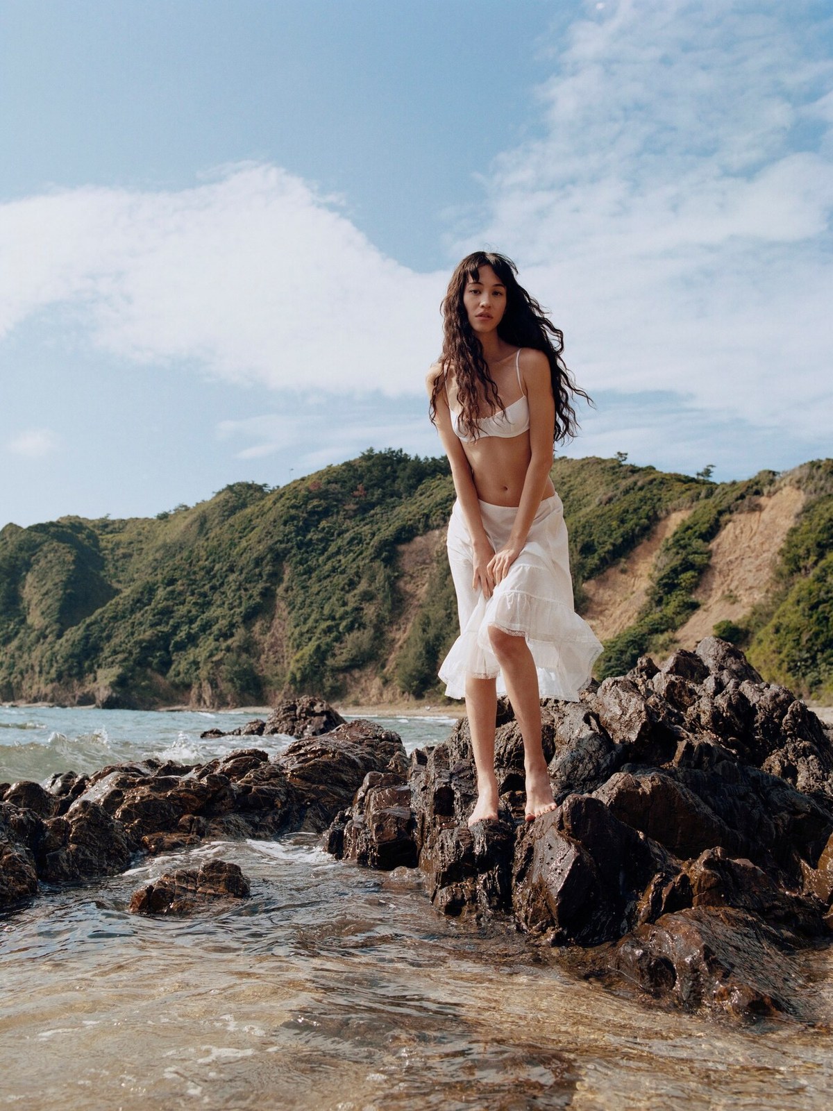 Kiko Mizuhara in a white Cou Cou slip on a rocky coastline