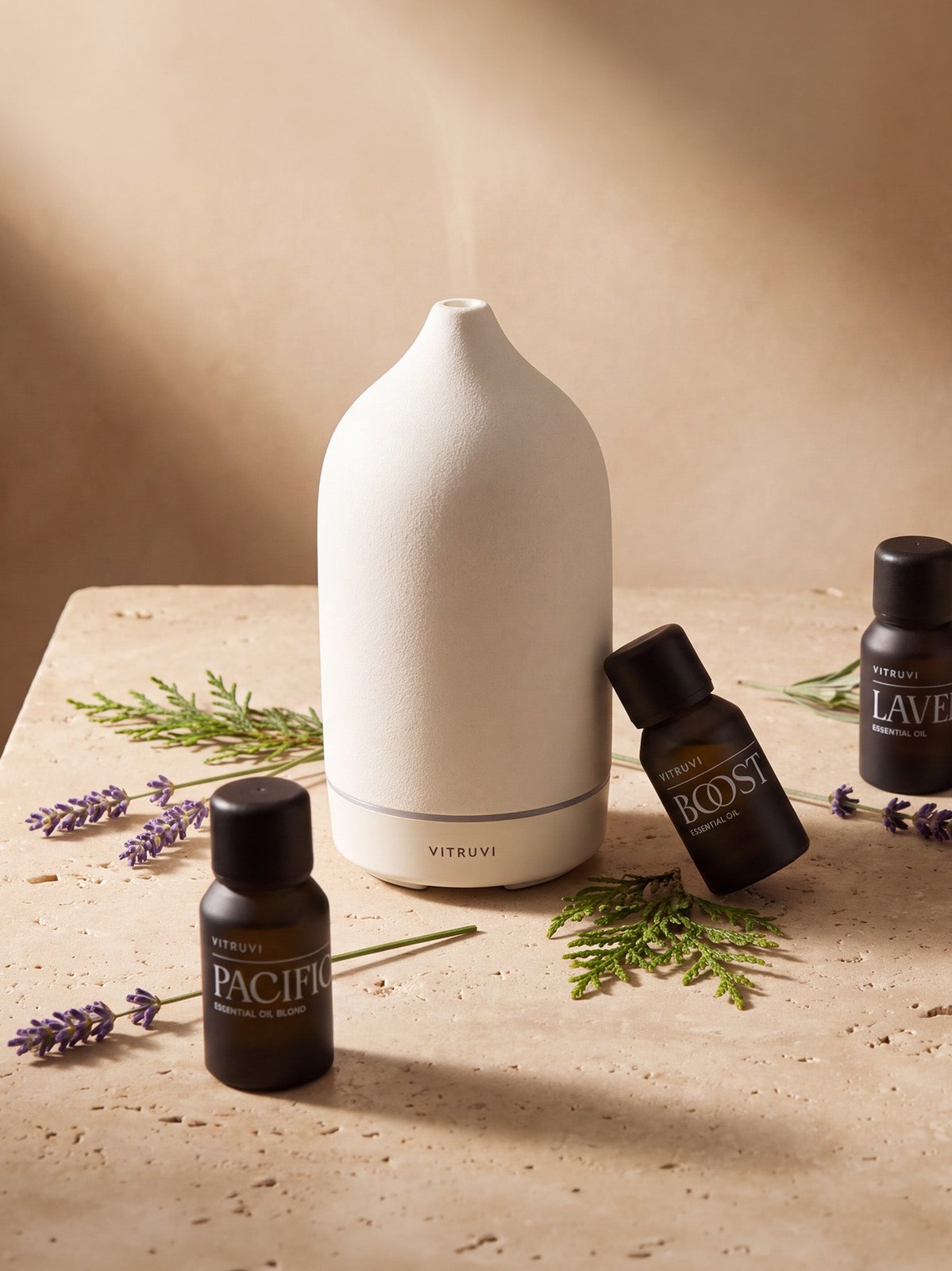 Vitruvi diffuser and essential oil bottles styled with lavender and greenery on a stone table