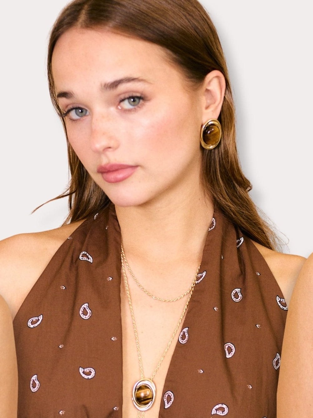 Model in a white top wearing a long bolo necklace and gold earrings