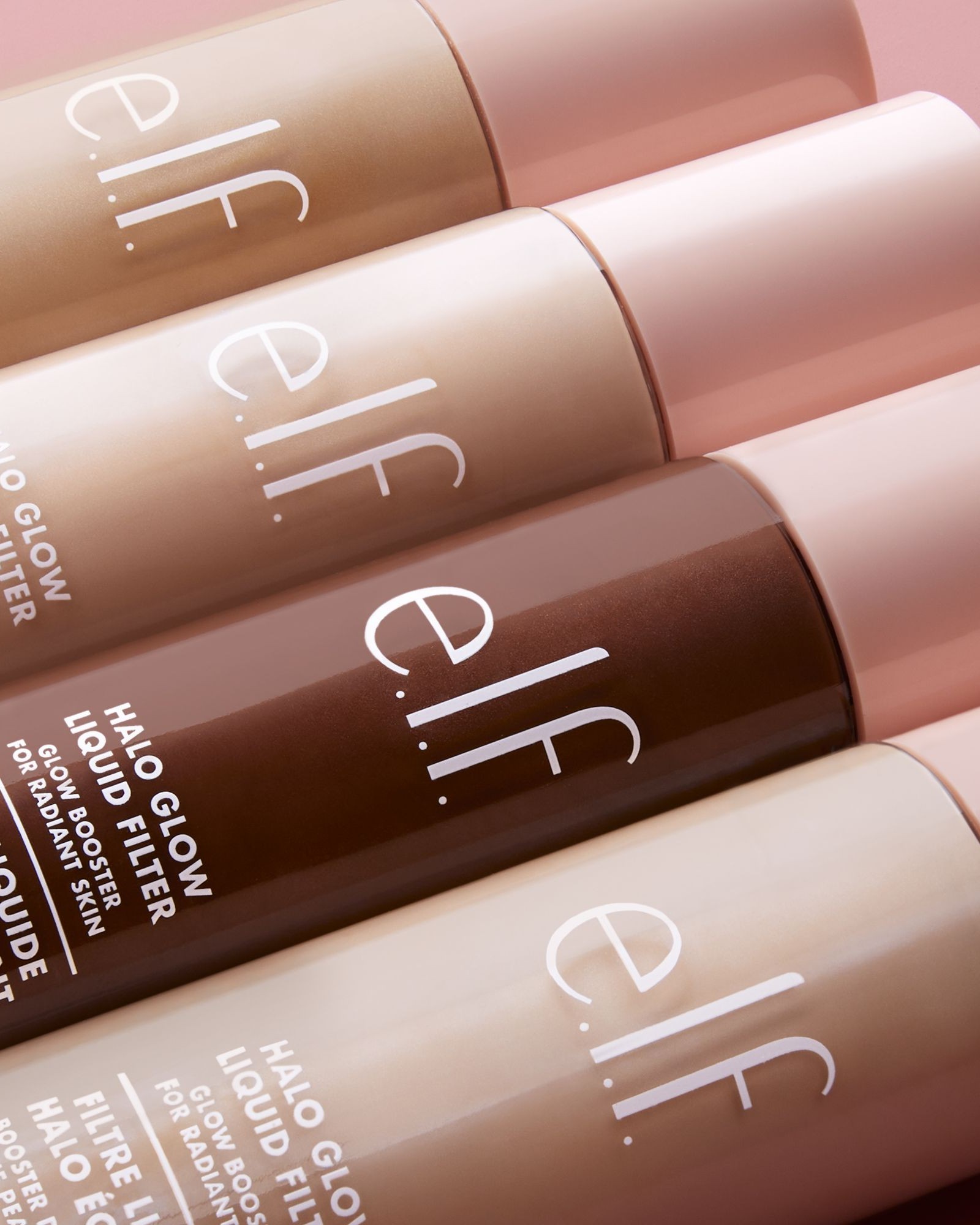 Close up of e.l.f. Halo Glow Liquid Filter bottles in several shades lying on a pink surface