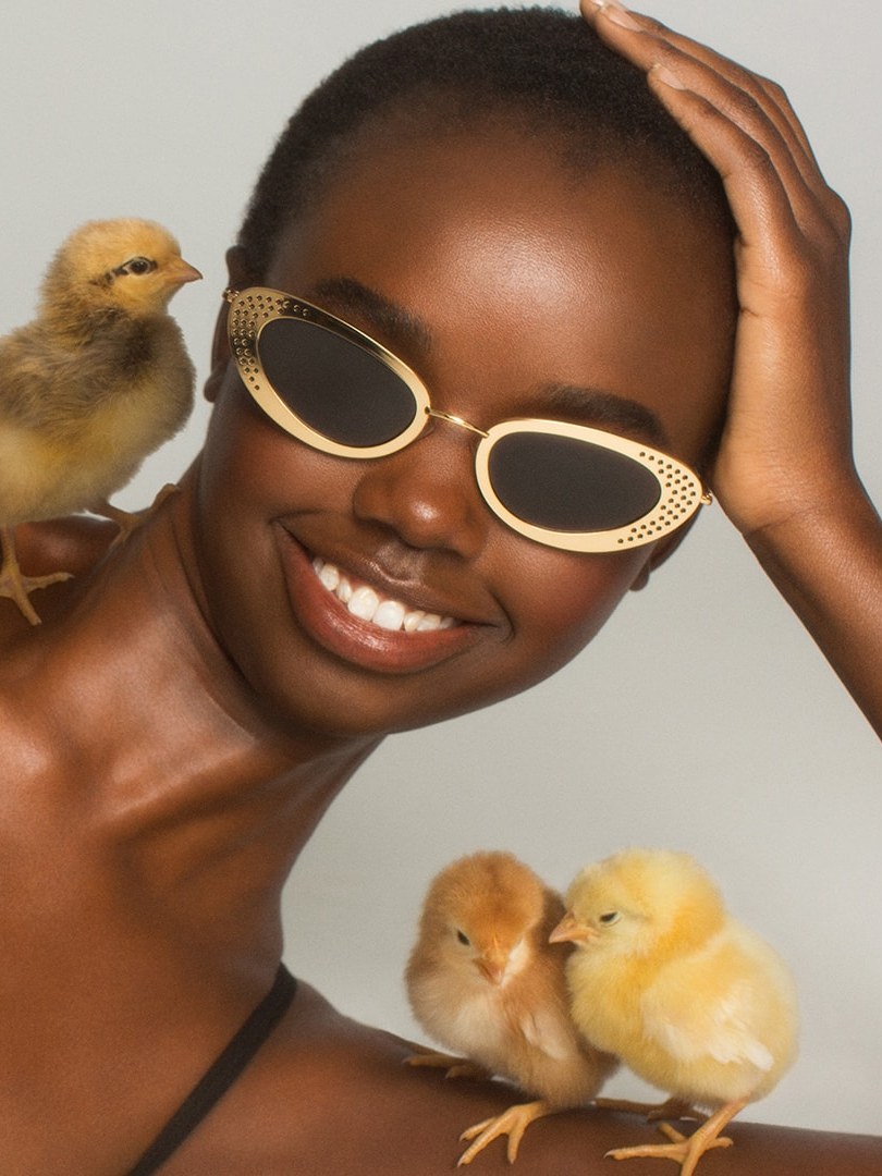 Smiling model in gold sunglasses with small chicks around her
