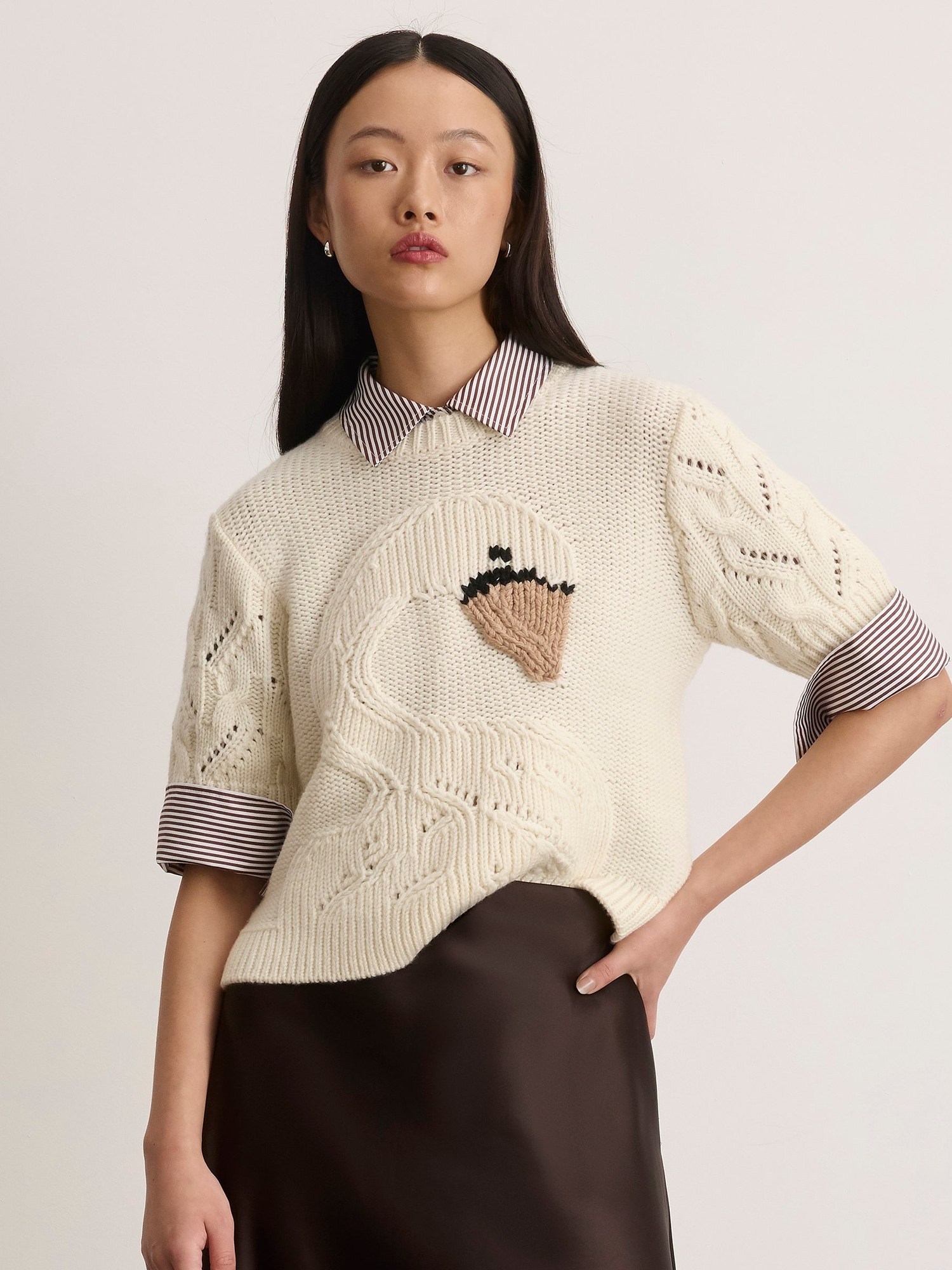 Model in a cream knit sweater with a swan motif over a brown skirt