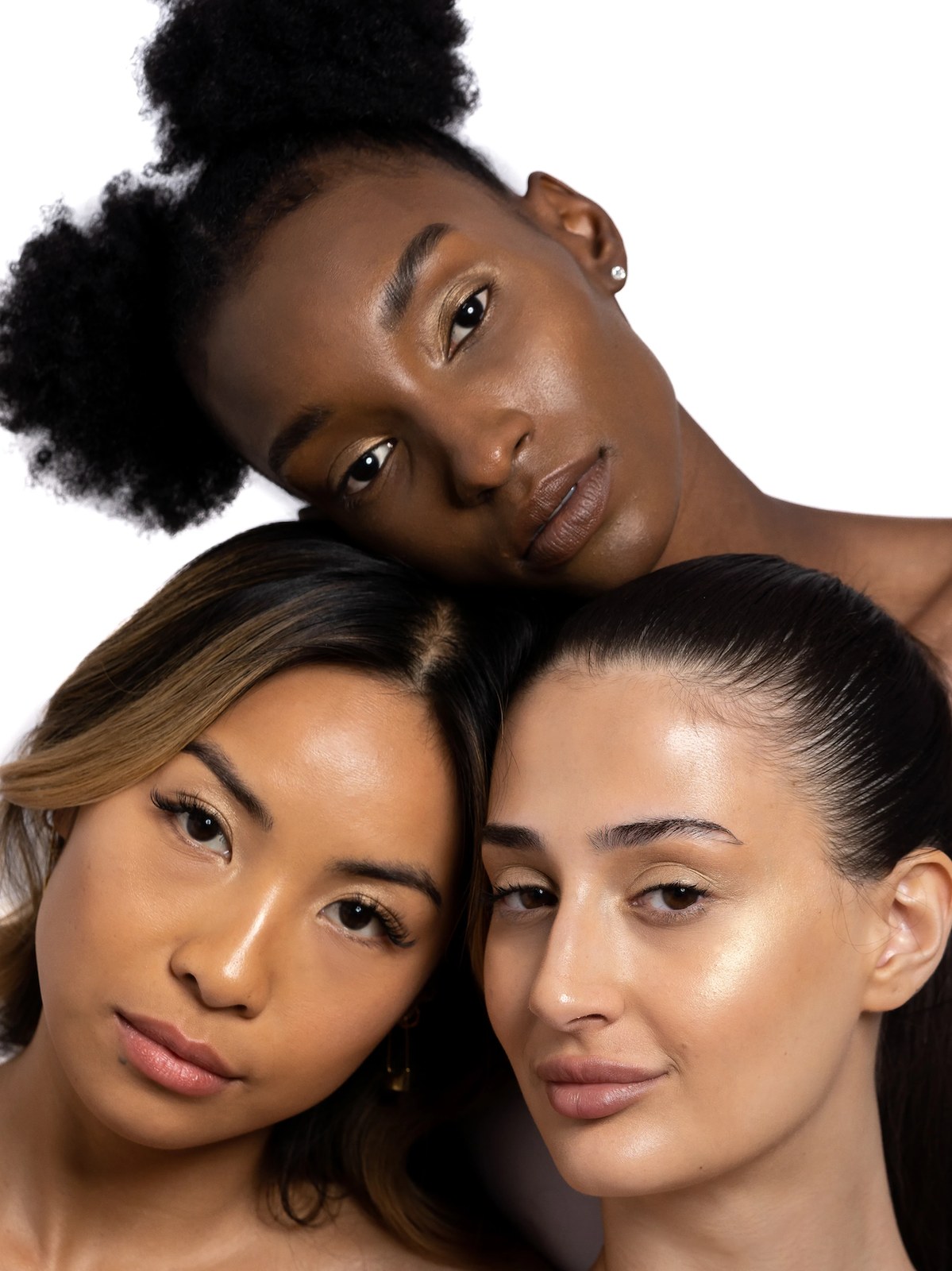 Three models with natural makeup arranged together in a bright studio portrait