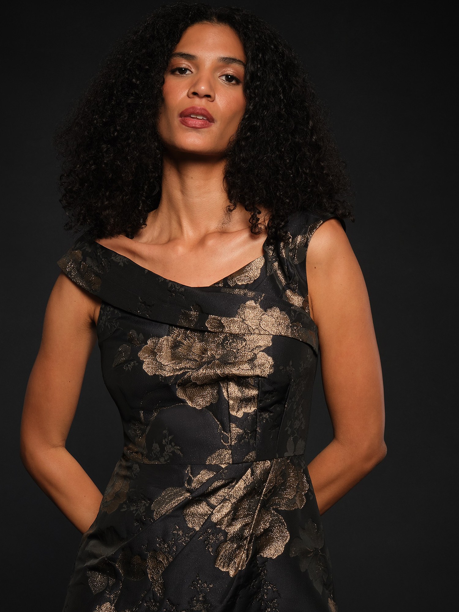Model in a black and gold floral jacquard off the shoulder dress