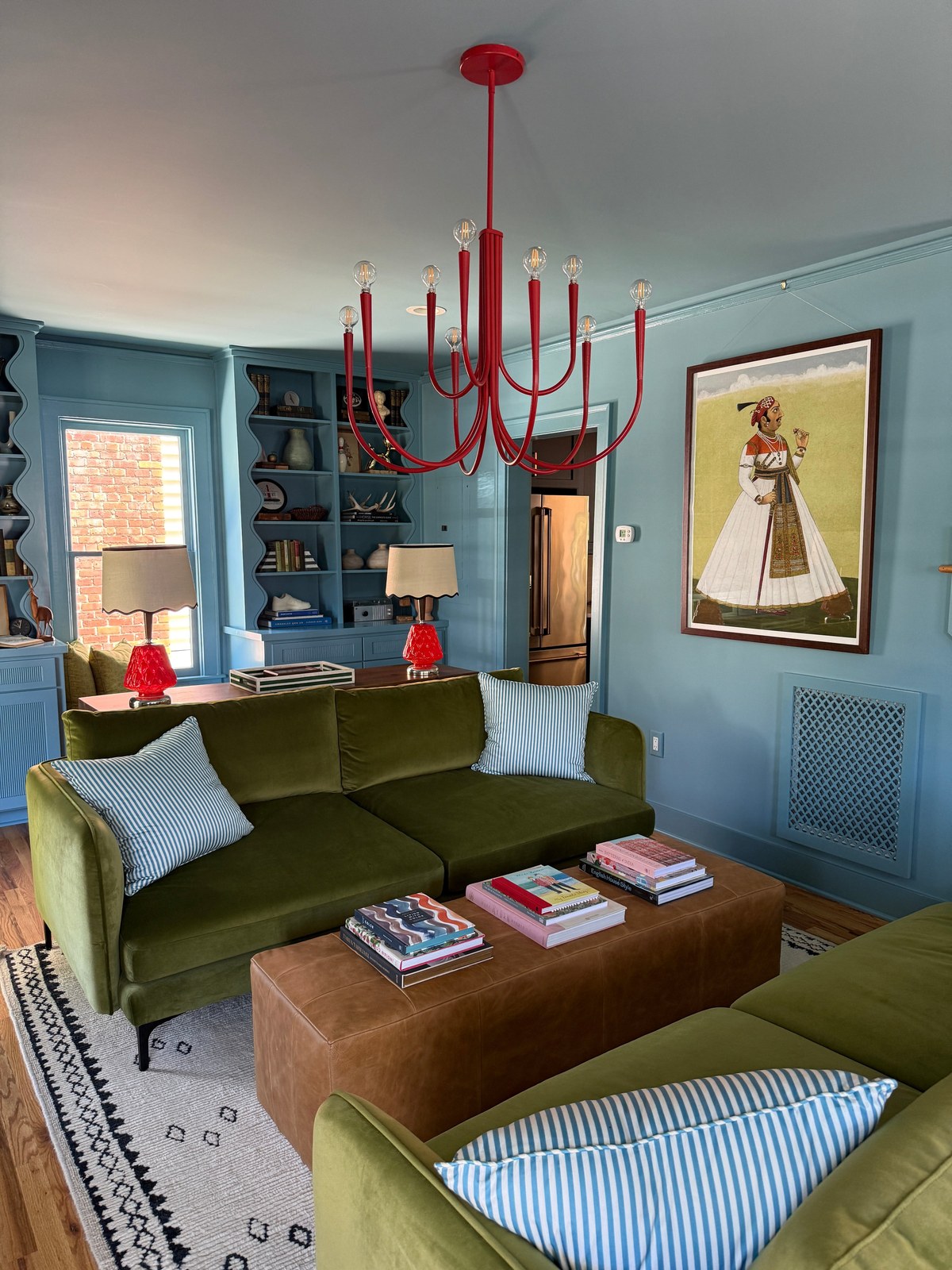 Blue living room with a green velvet sofa and a red chandelier