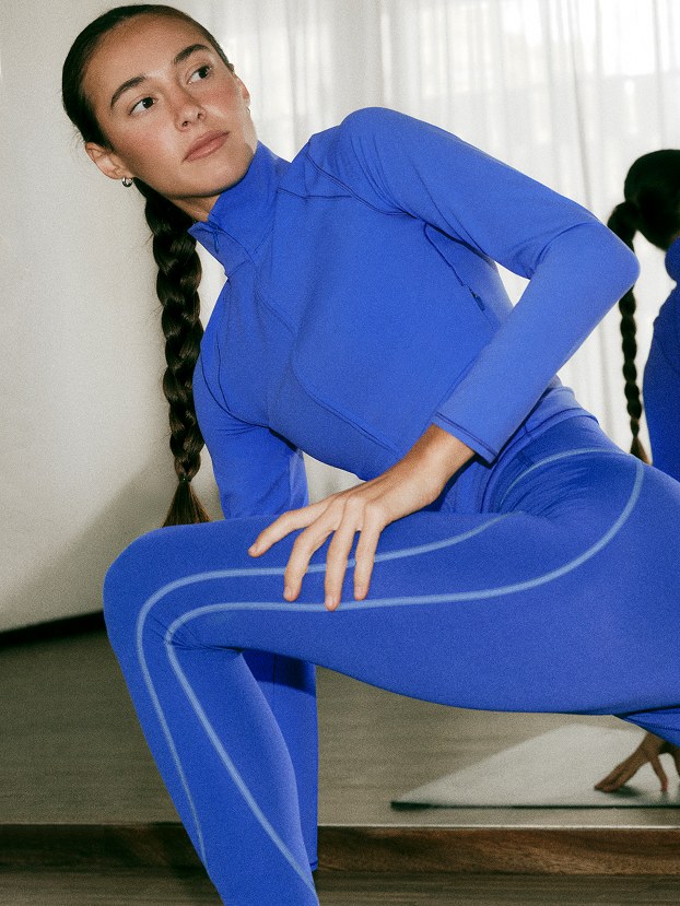 Woman in cobalt training clothes holding a low exercise pose in a studio