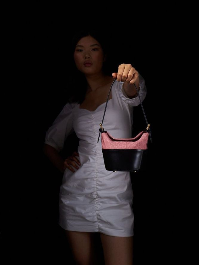 Model in a white dress holding a two-tone BY FAR shoulder bag in a dark studio