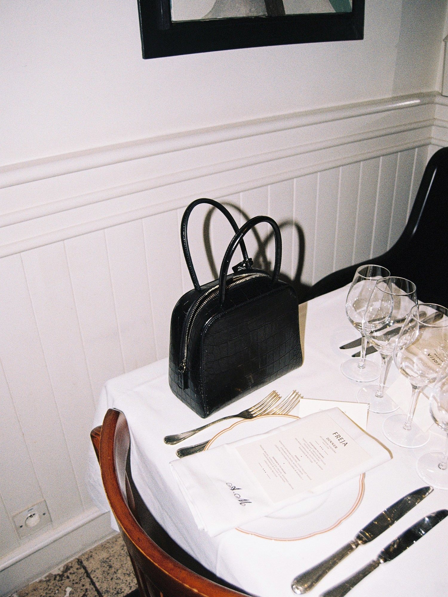 Black croc texture Freja bag on a restaurant table set with glasses