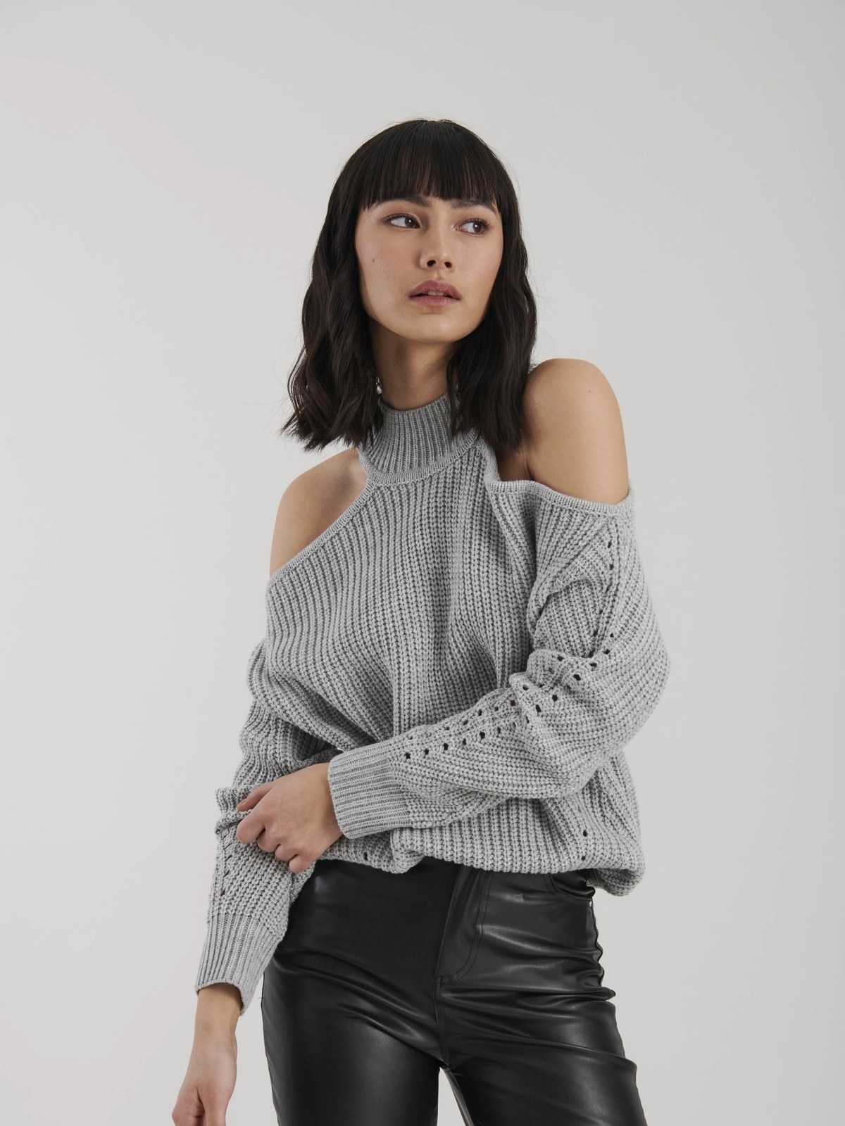 Model wearing a light gray cold-shoulder sweater with black trousers