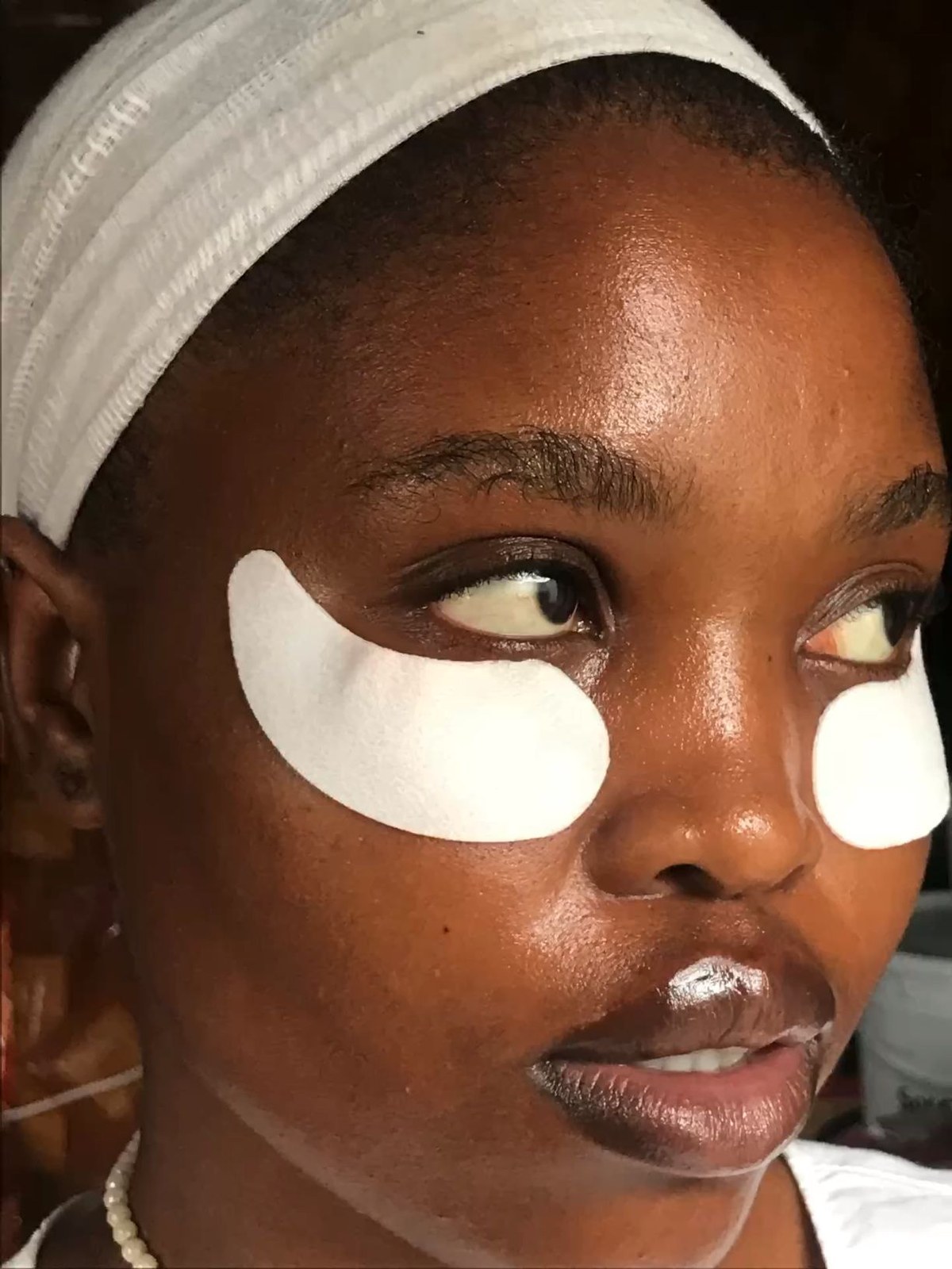 Woman in a white headband wearing white under-eye patches and glancing to the side
