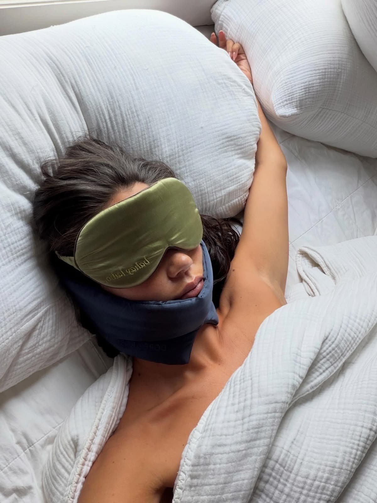 Hand holding a green silk scrunchie and matching eye mask against a beige background