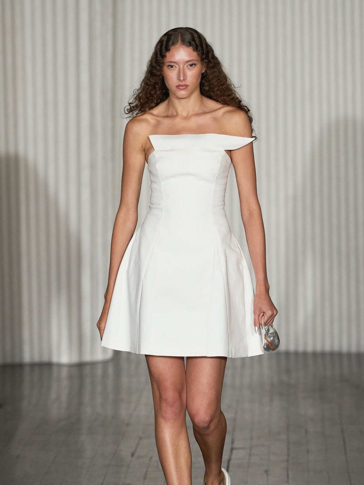 Model in a sculpted white mini dress walking a runway