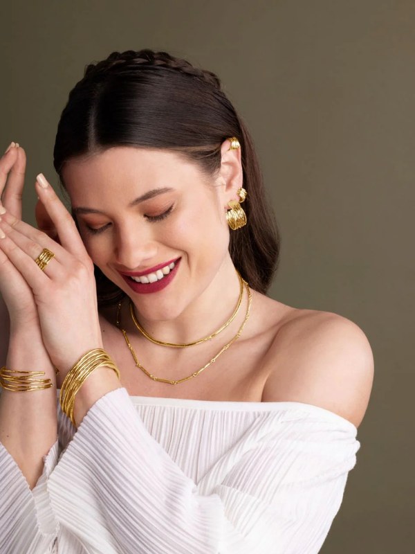 Model in a white top wearing layered gold SOKO necklaces and bracelets