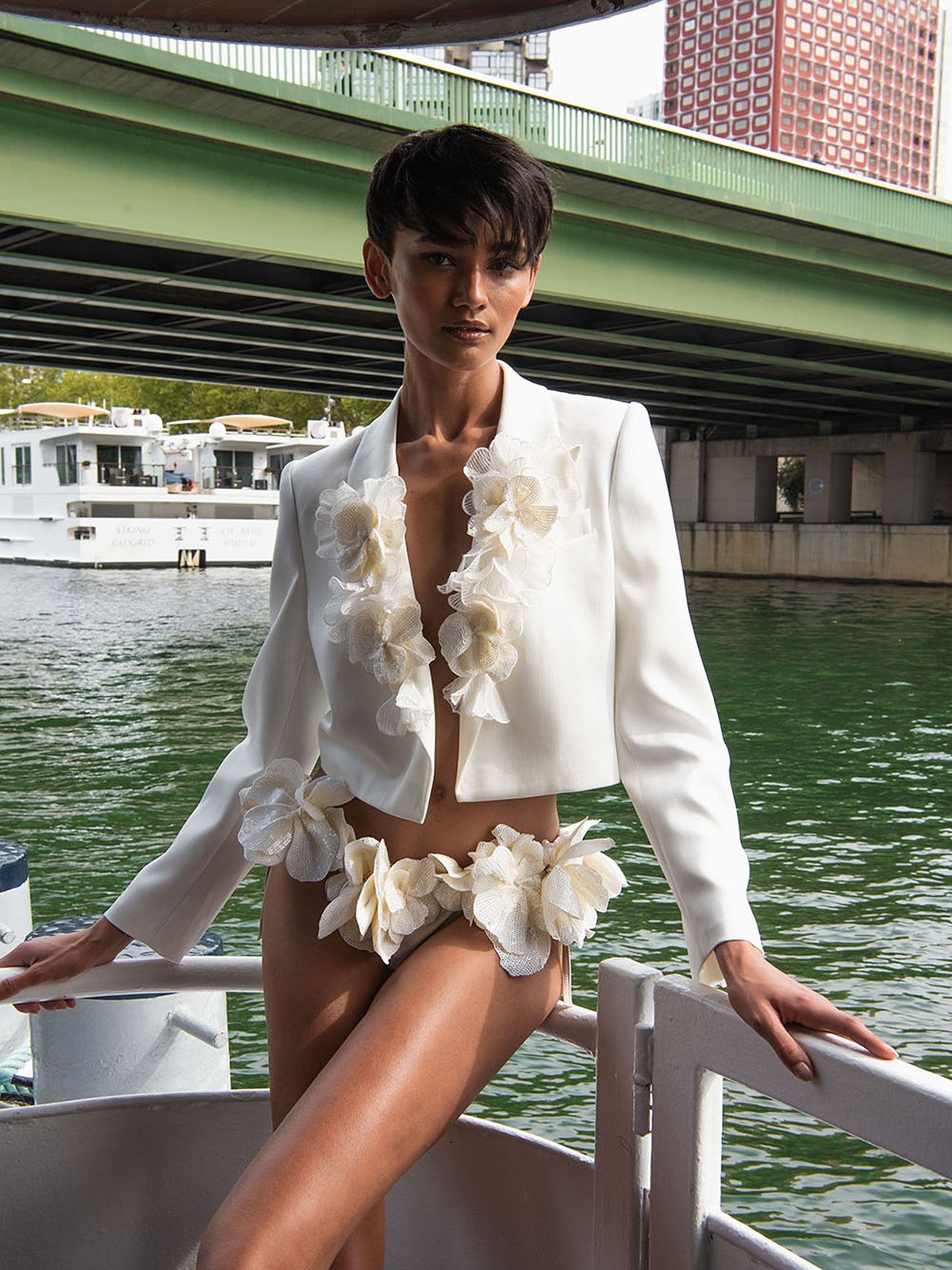 Model in a cropped white blazer and shorts with ivory floral appliques on a Seine boat