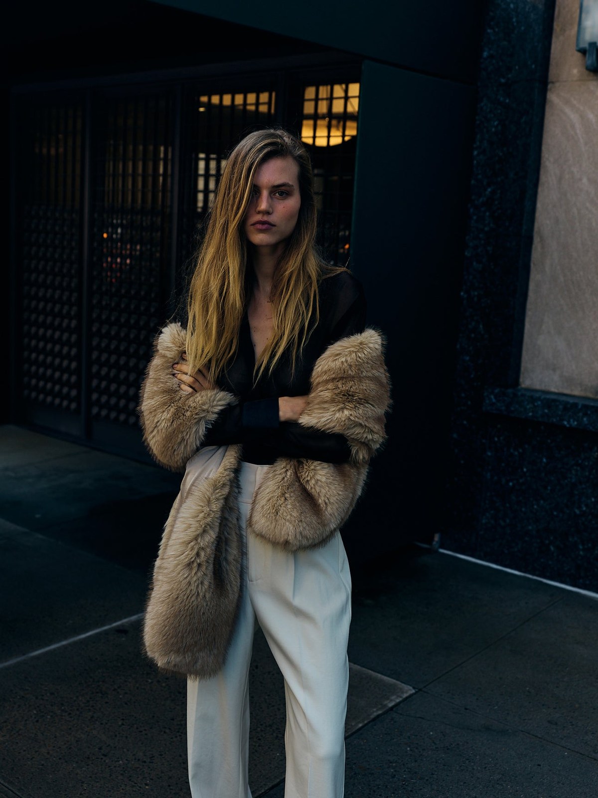 Model in a dark top and pale trousers on a city sidewalk