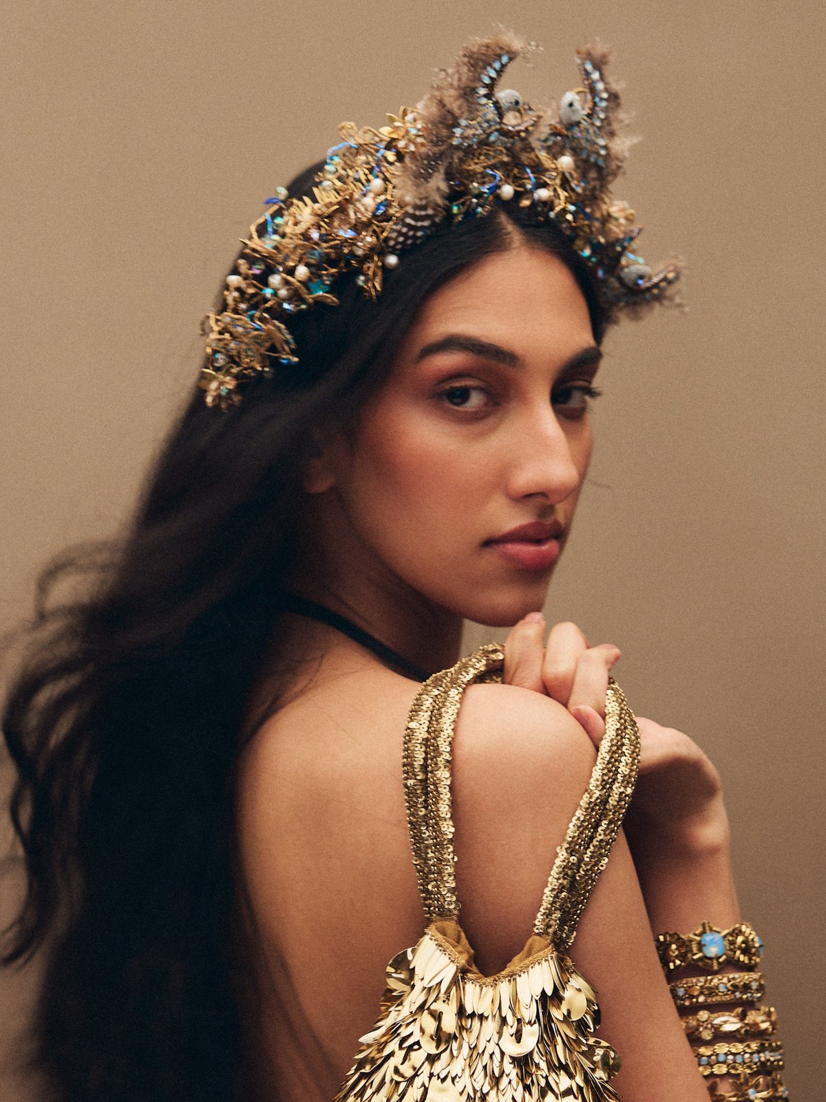 Model in a gold and ivory statement dress and matching necklace against a warm studio backdrop