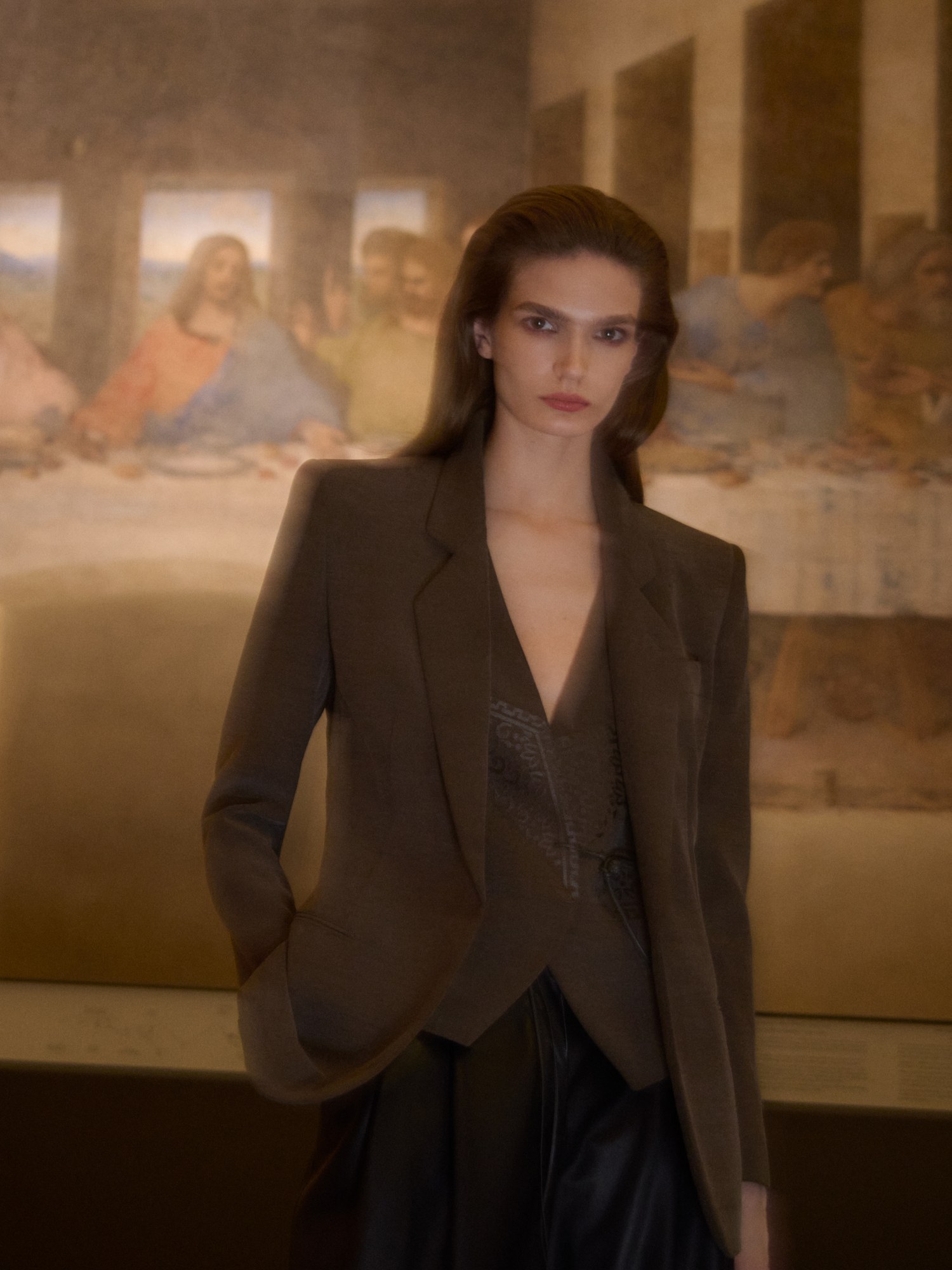 Model in an olive brown blazer and waistcoat in a gallery in front of a mural