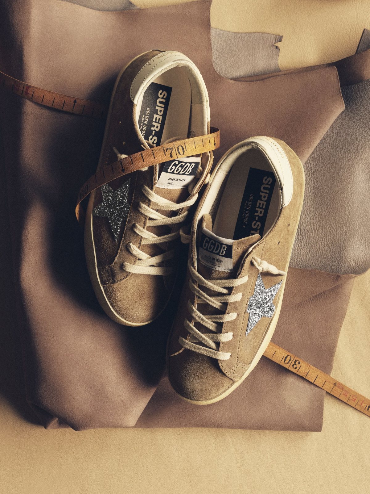 Golden Goose Super-Star sneakers with glitter stars on a sand coloured backdrop