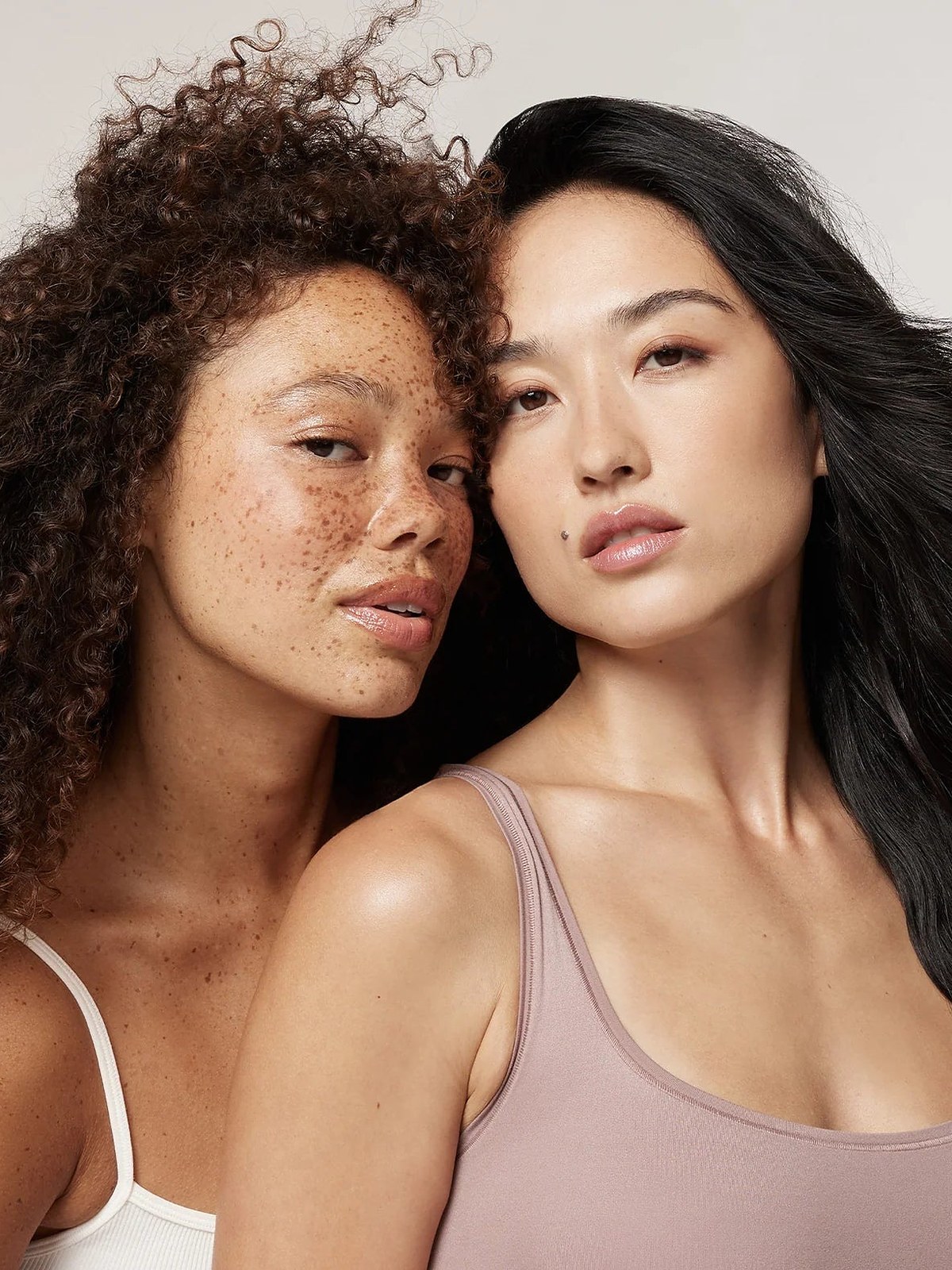 Two women, one with curly hair and one with long black hair, in tank tops