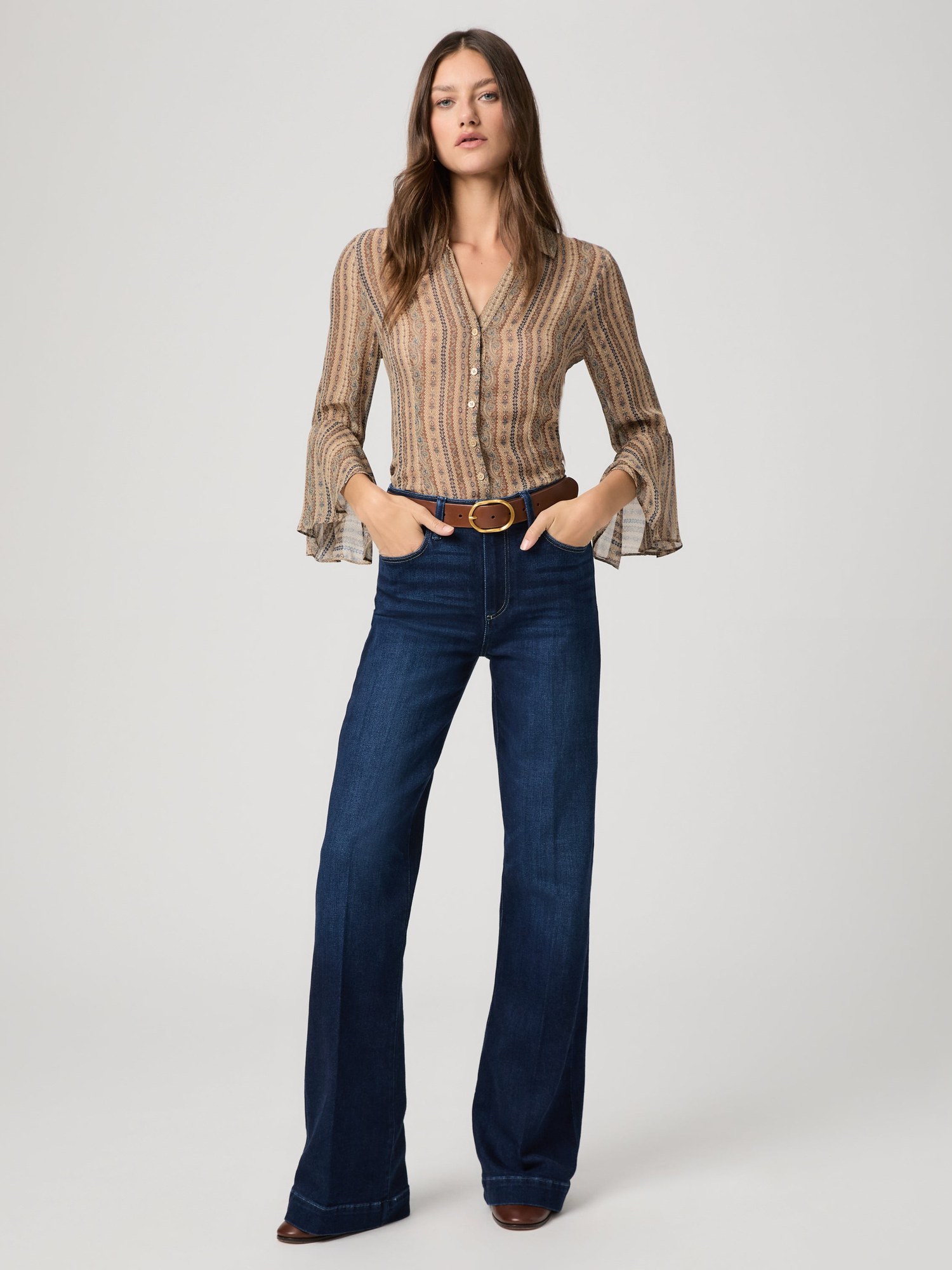 Model in a striped bell sleeve blouse and dark flared jeans on a grey studio backdrop