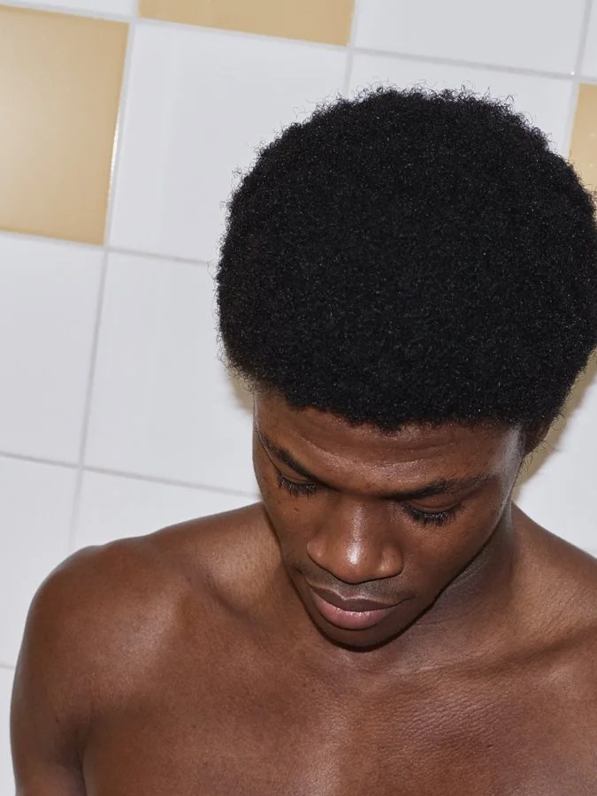 Man in a tiled bathroom looking down during a skincare campaign