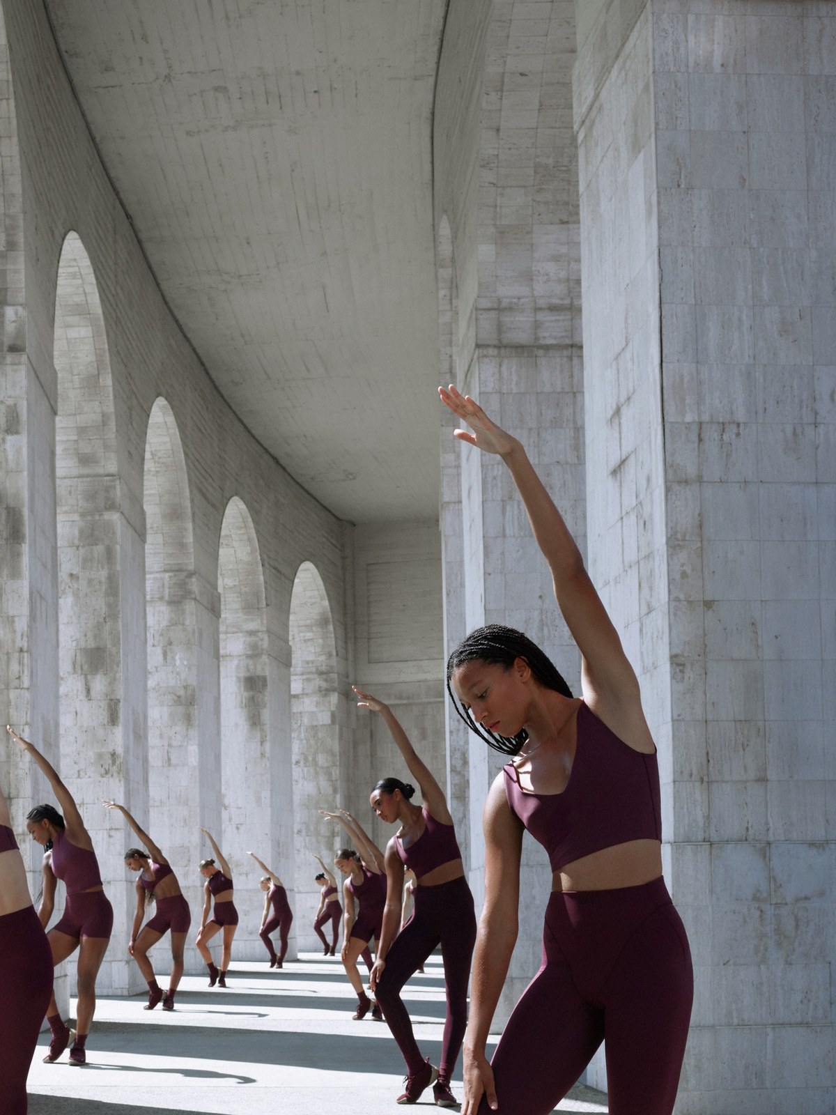 NikeSKIMS athletes stretch in wine-colored training sets beneath pale stone arches