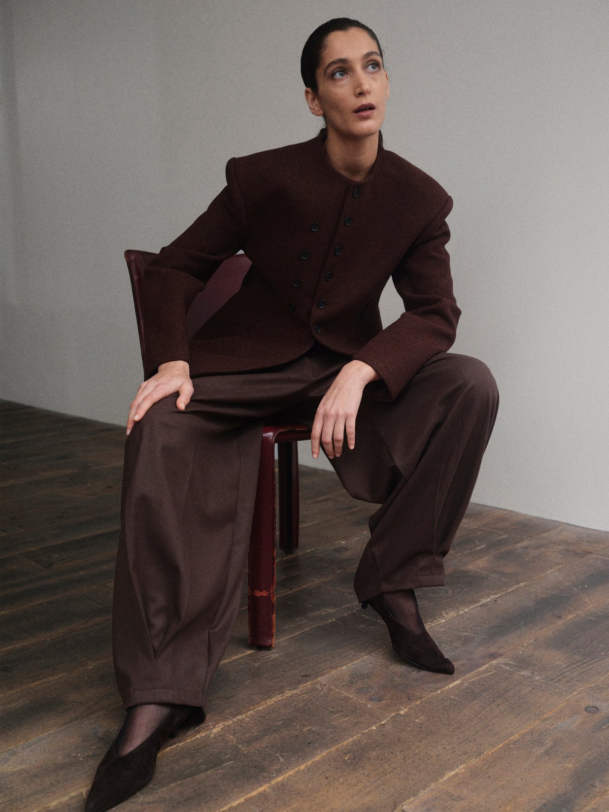 Model in a dark brown tailored suit seated on a studio chair