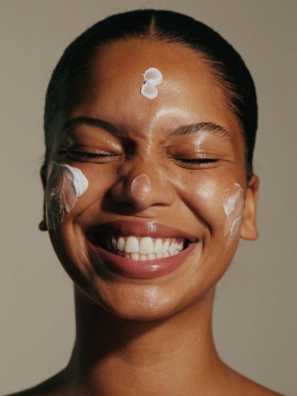 Close-up of a smiling woman with dots of white moisturizer on her forehead and cheeks