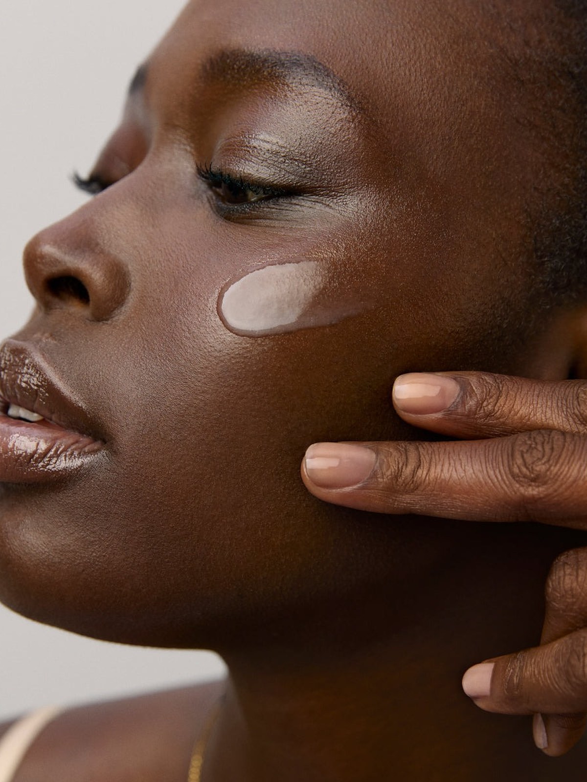 Model in profile with a skincare swatch on her cheek and a hand at her jaw