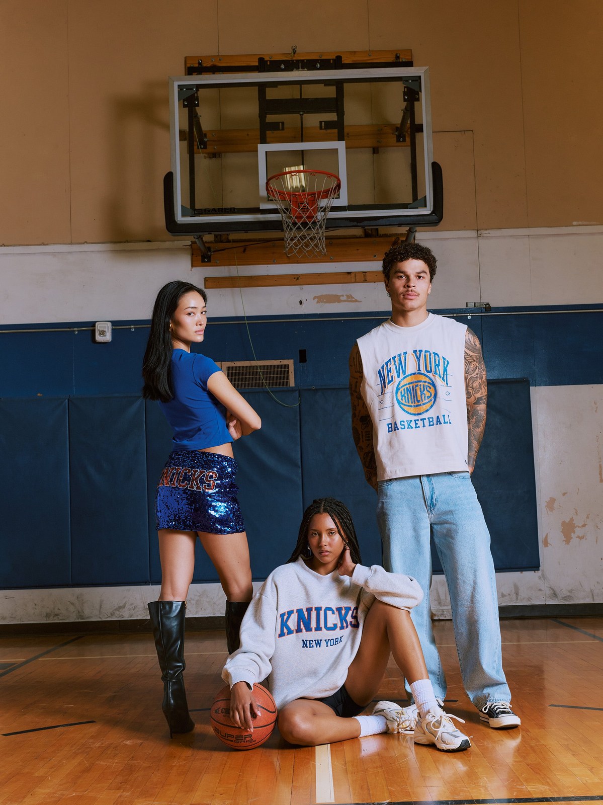 Three models in Knicks fanwear on a basketball court