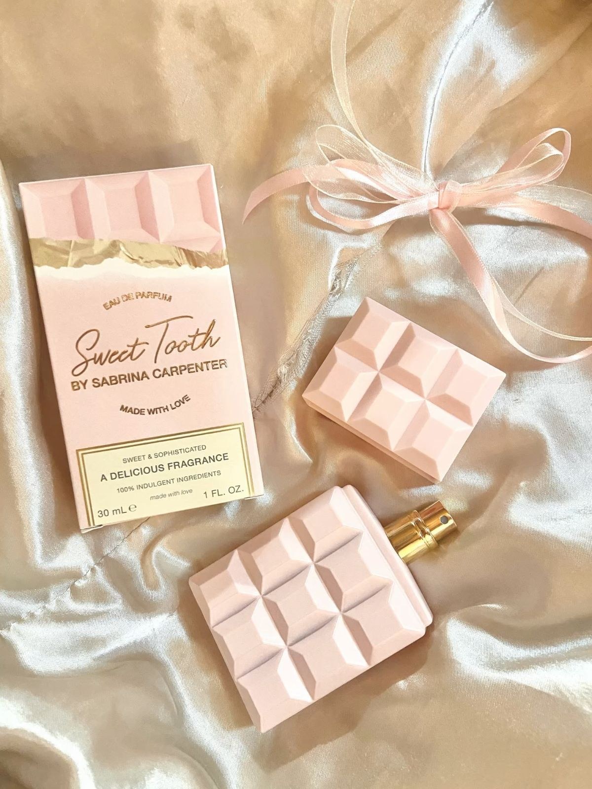 Pale pink chocolate-bar perfume bottle and box on cream satin beside a pink ribbon bow