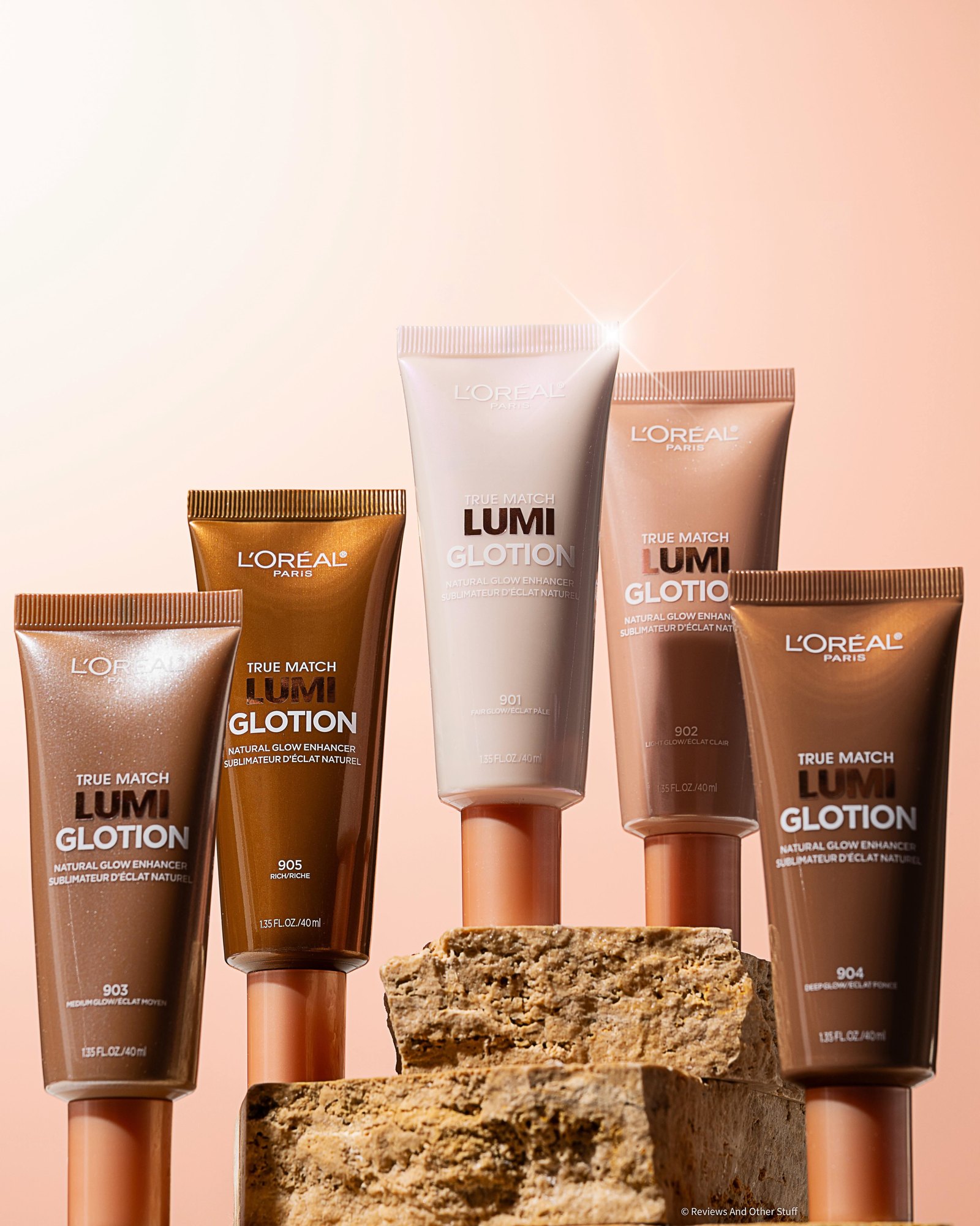 Five L'Oréal Paris True Match Lumi Glotion tubes in shades 901 to 905, from pale pearl to deep bronze, standing on stone blocks against a peach gradient background.